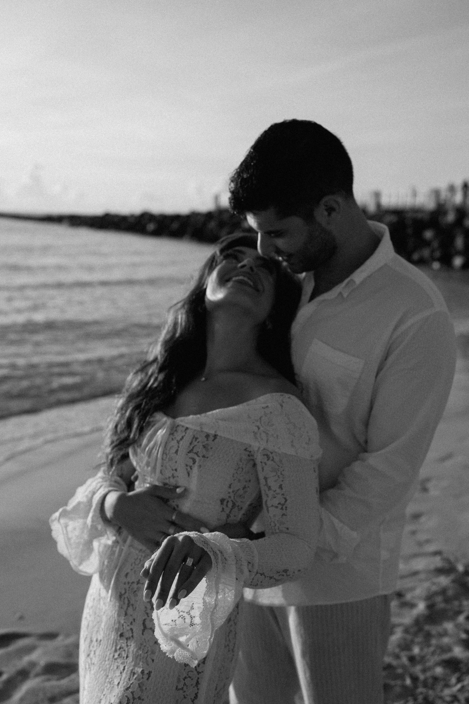 A romantic black and white photo of a couple embracing on the beach at sunset.