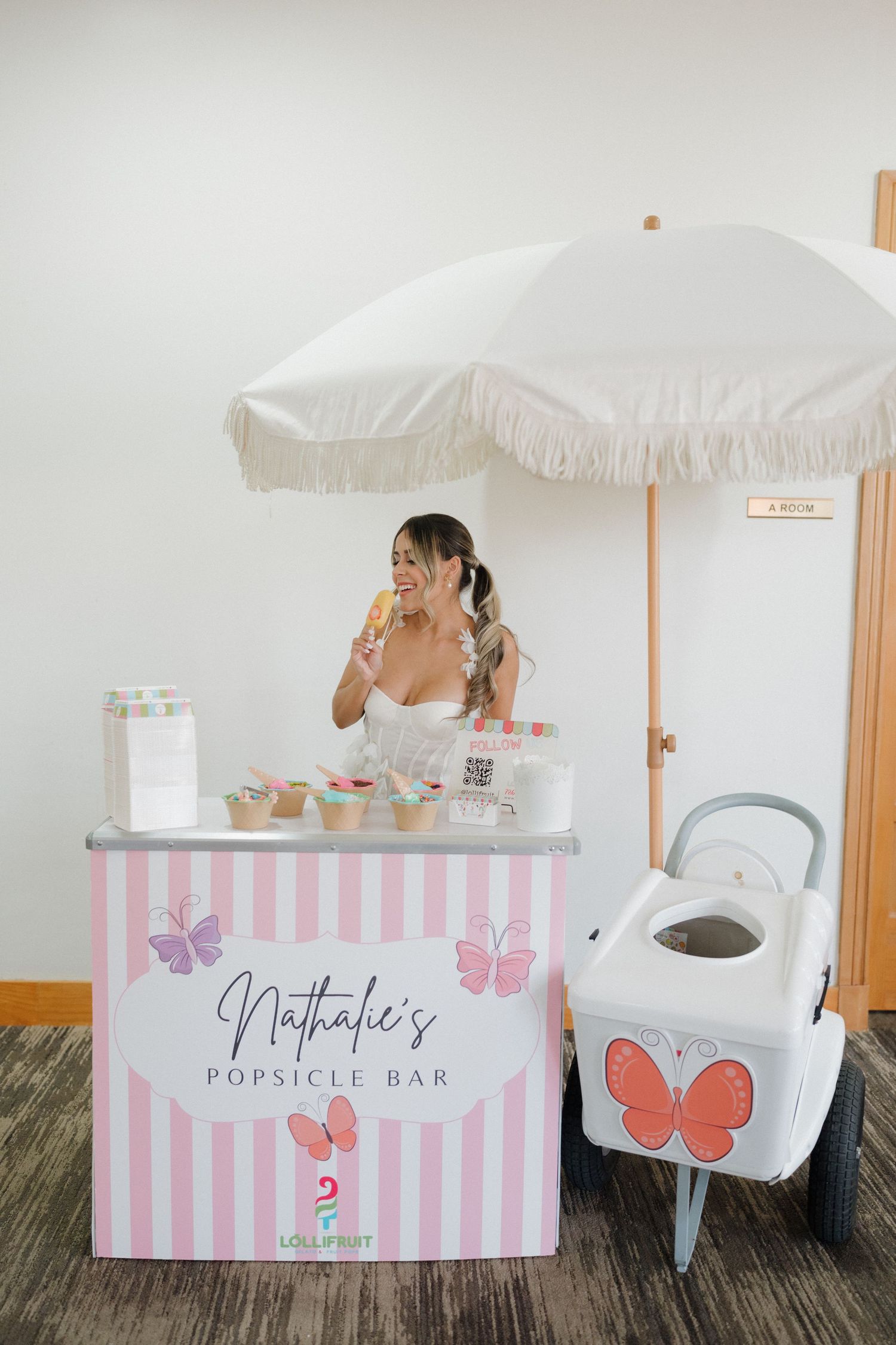Pink and white striped punch bar cart with butterfly decorations and white umbrella.