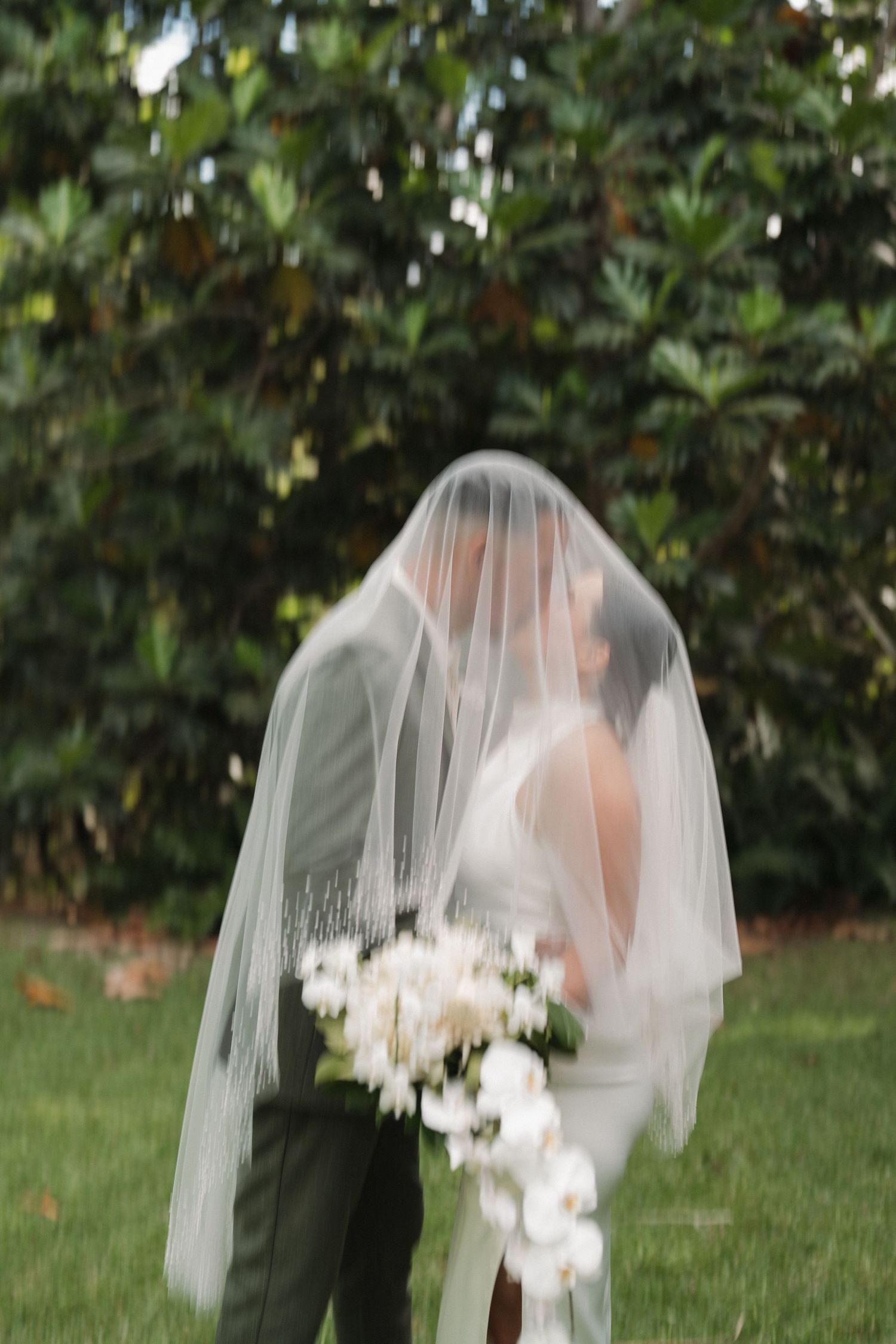 A romantic wedding portrait through a flowing veil with white flowers in the garden.