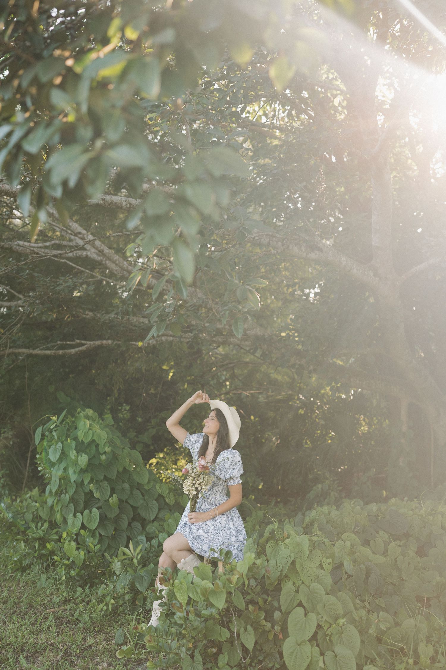 Dreamy sunlit garden scene with flowy dress and hat in natural setting.
