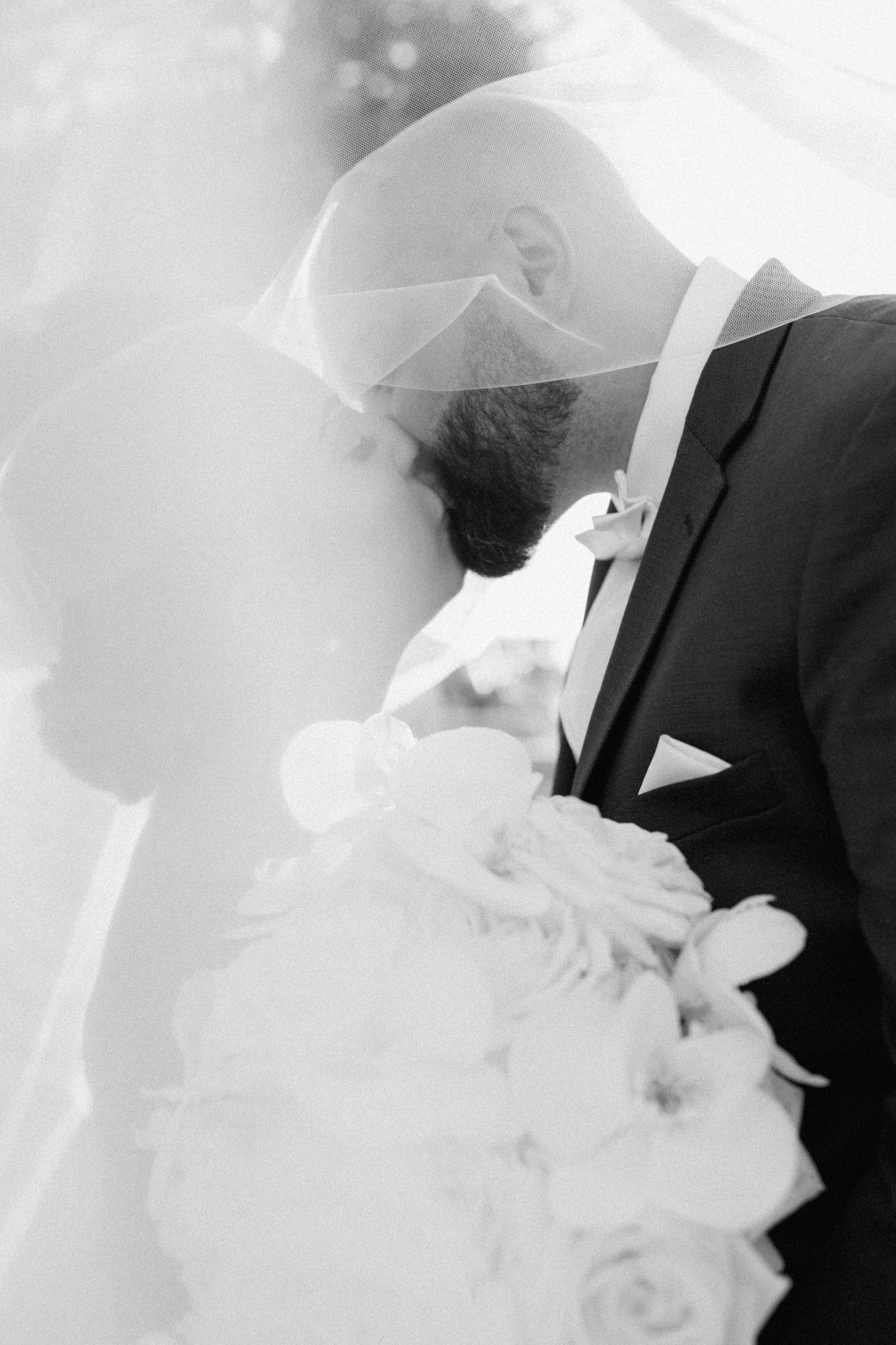 Black and white close-up of romantic wedding moment under flowing veil.