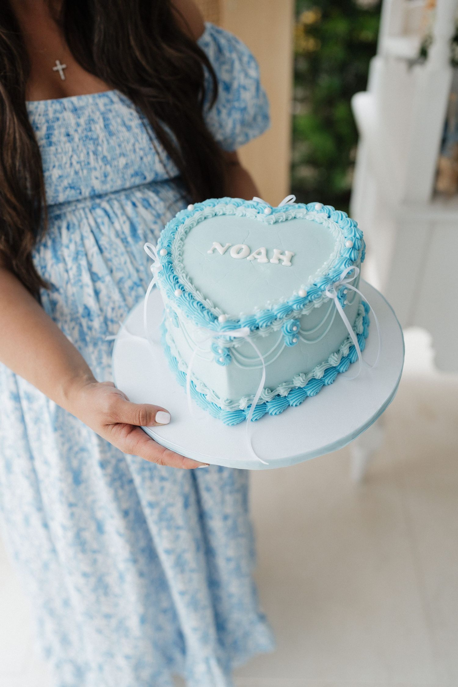 Light blue frosted cake with delicate piping details held against matching floral dress.