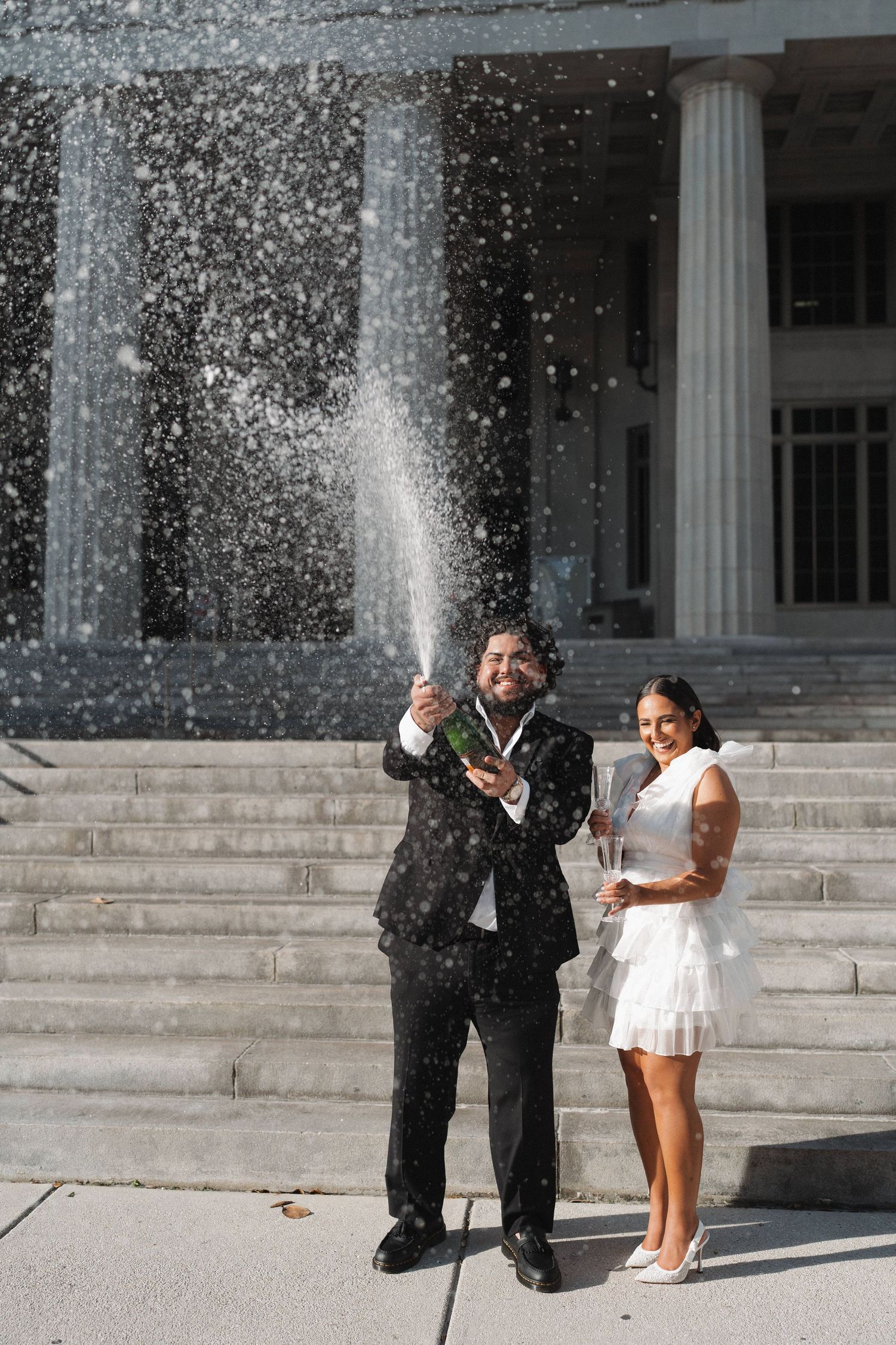A celebratory moment with champagne spray in front of a classical building facade.