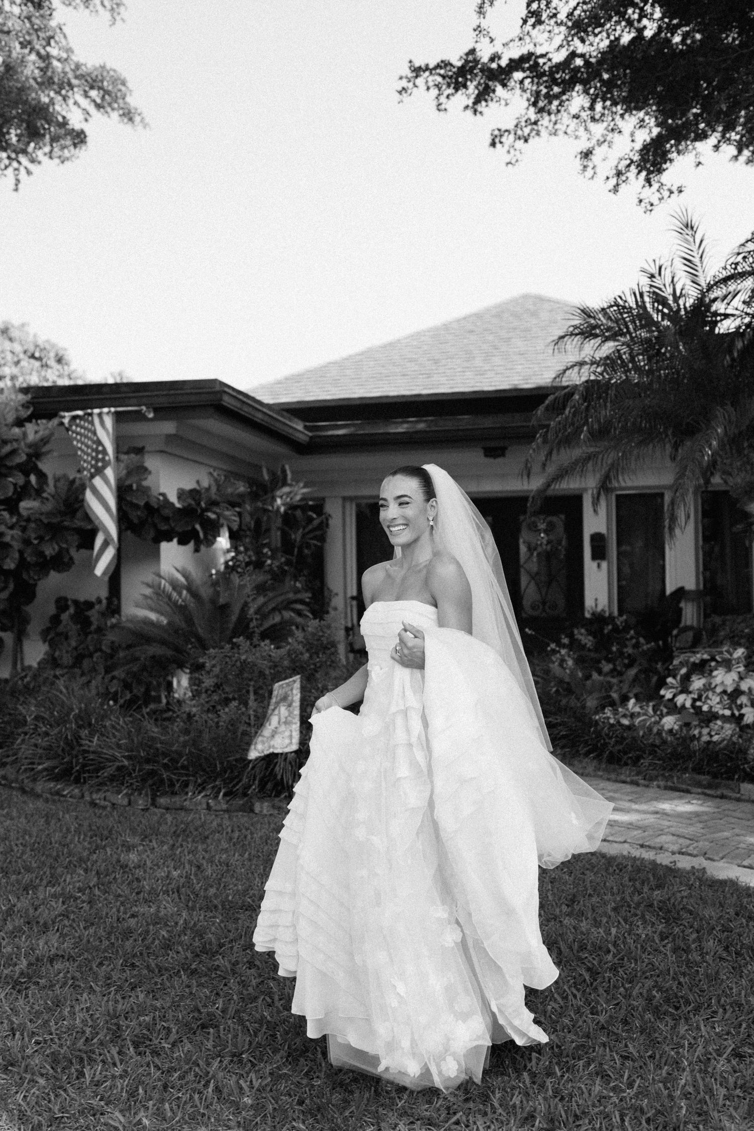 Bride in flowing white gown poses in front of house with palm trees.