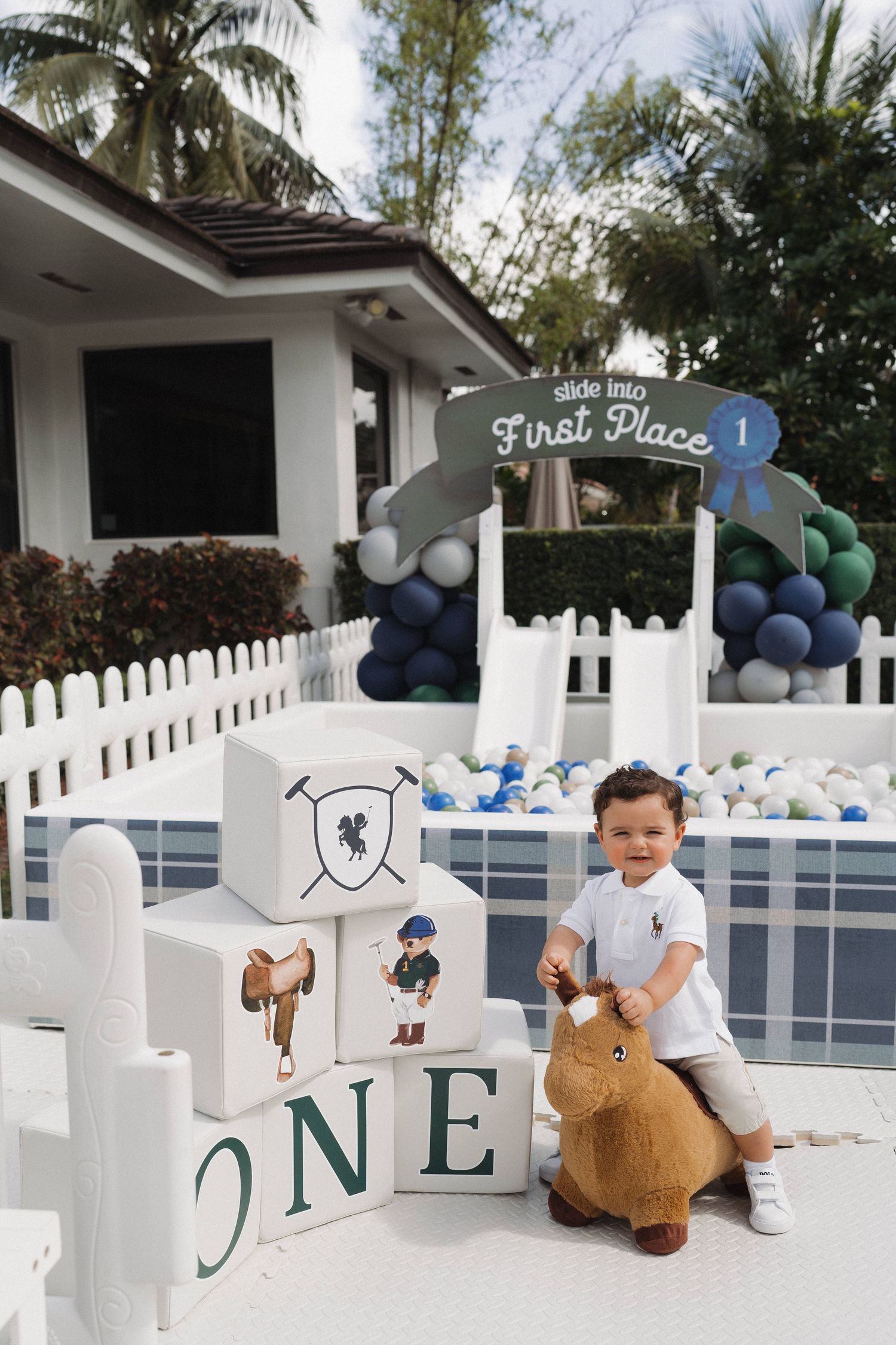First birthday party setup with white picket fence decorations and blue balloon garland.