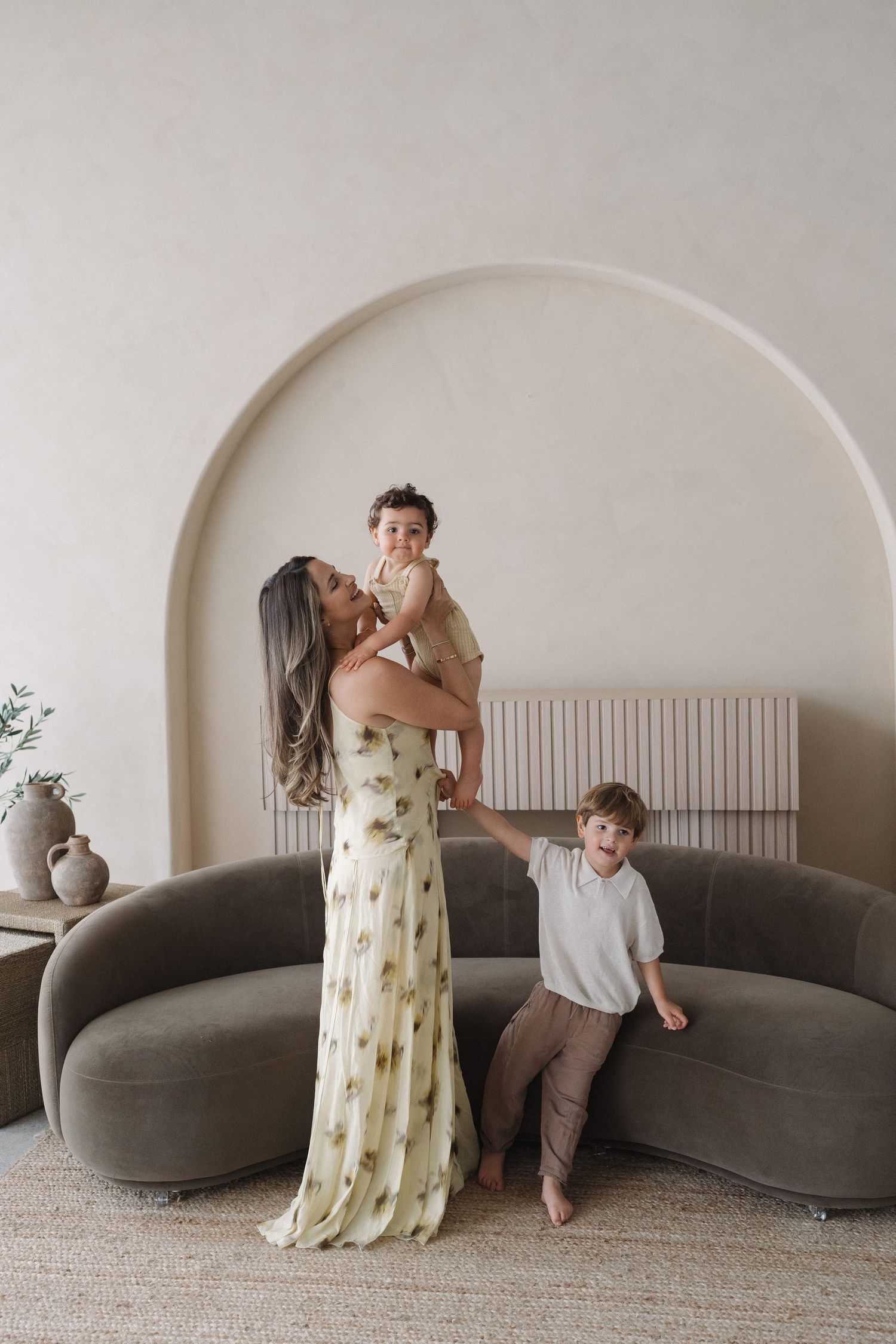 Family moment captured in minimalist room with curved grey sofa and arched wall.