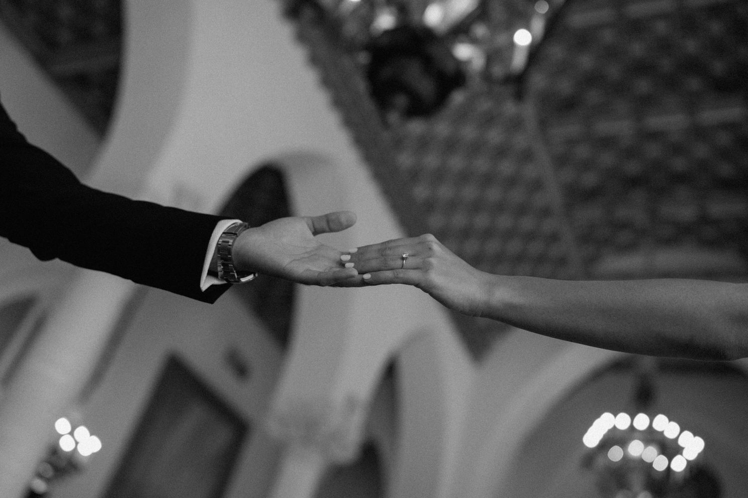 Black and white photo of two hands reaching towards each other under an ornate ceiling.