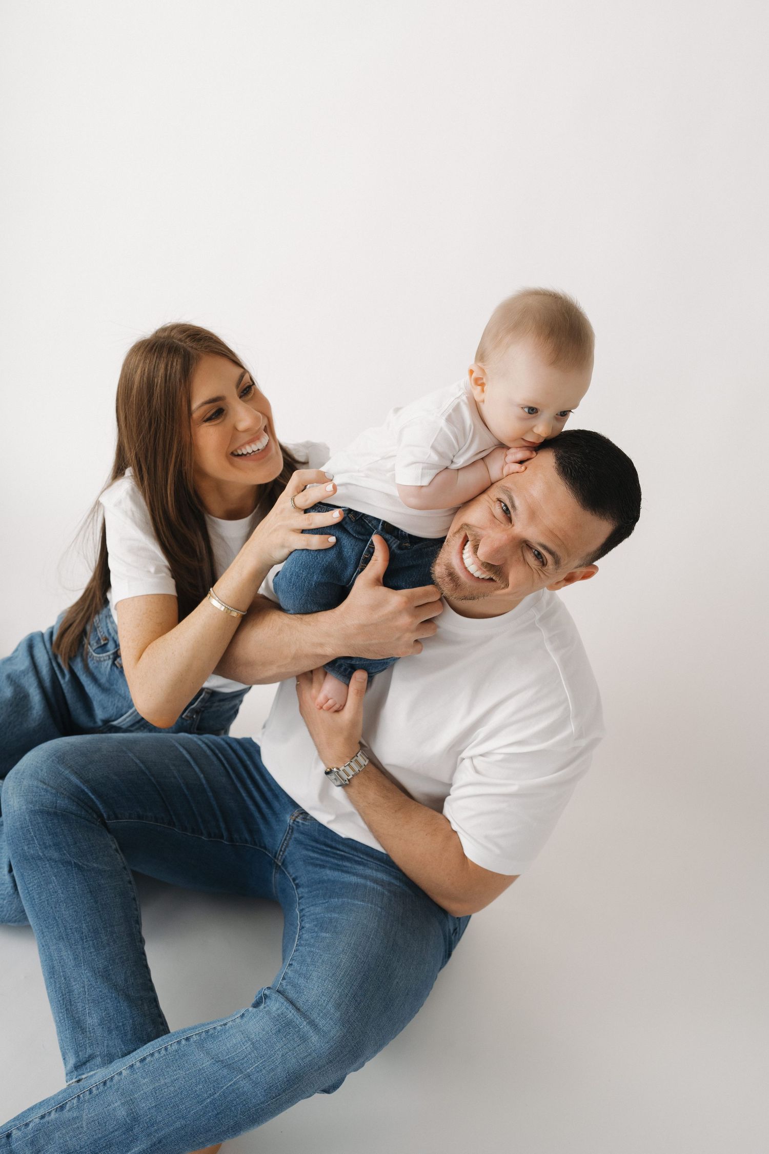 Candid family moment with parents and baby playing on white background.
