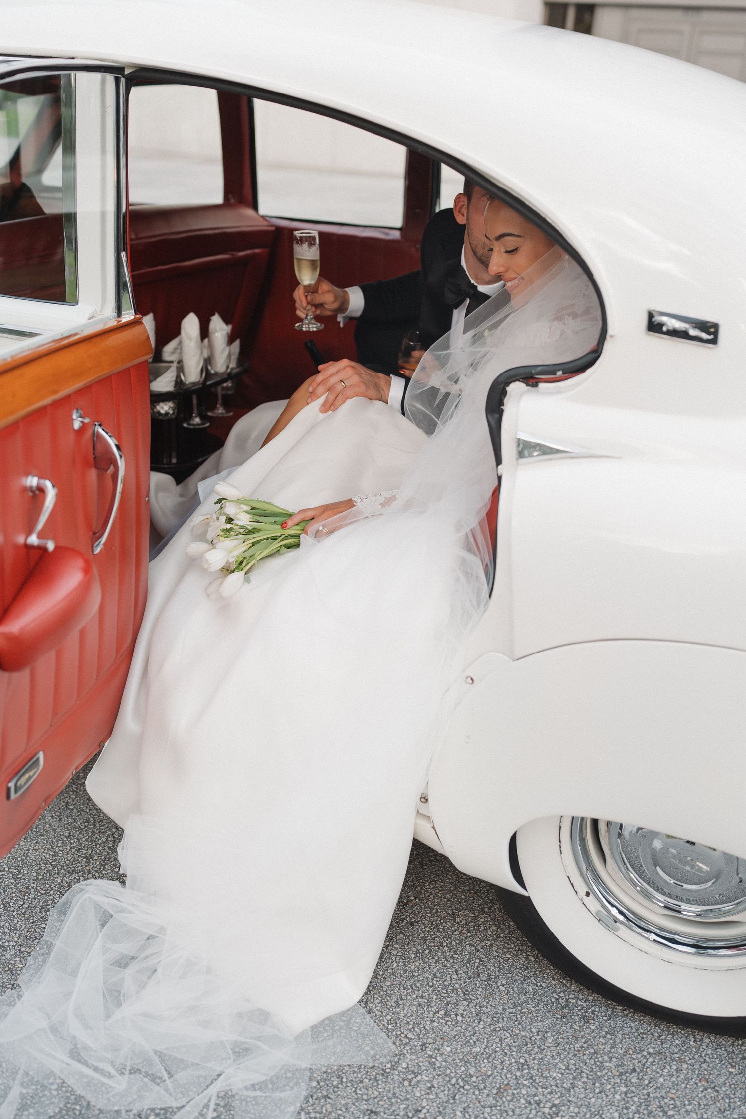 Wedding scene with classic white vintage car and flowing bridal gown.