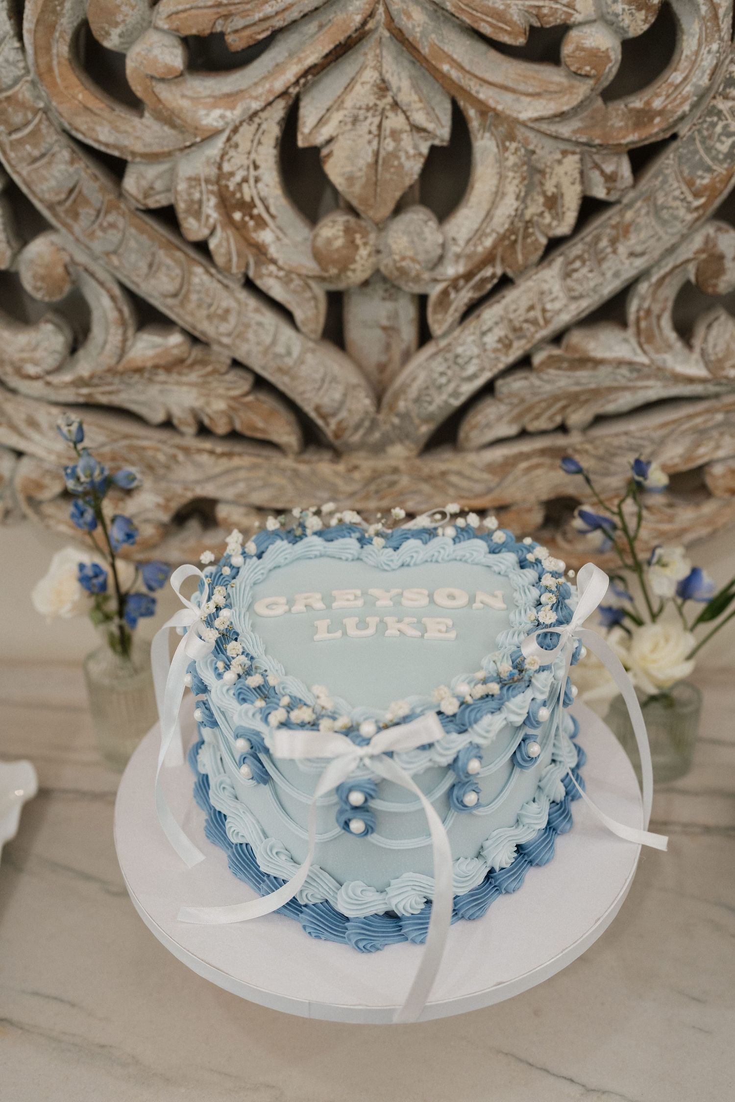 Light blue and white decorated cake with delicate floral details and ribbon accents.