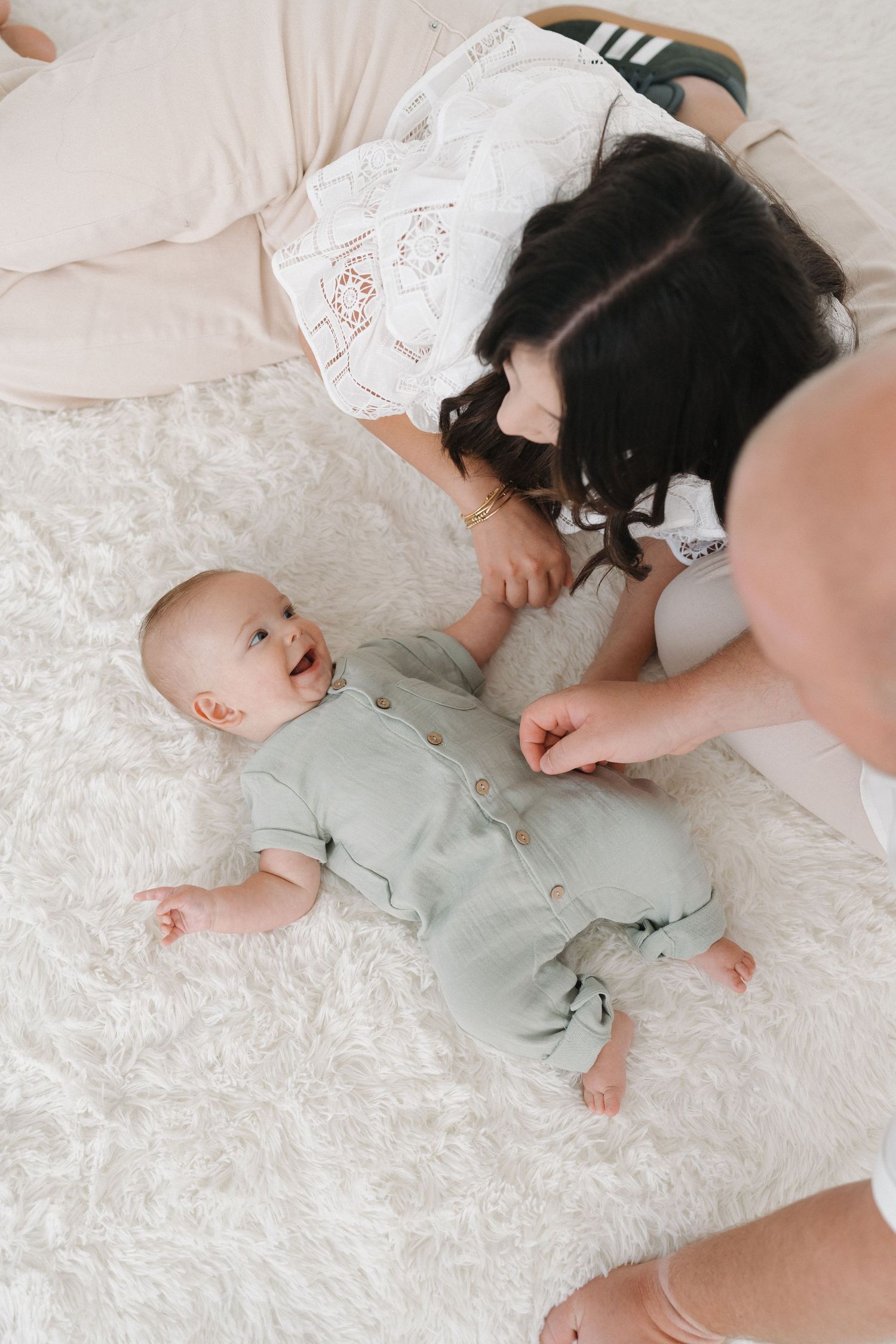 A smiling baby lying on white bedding while being cared for.