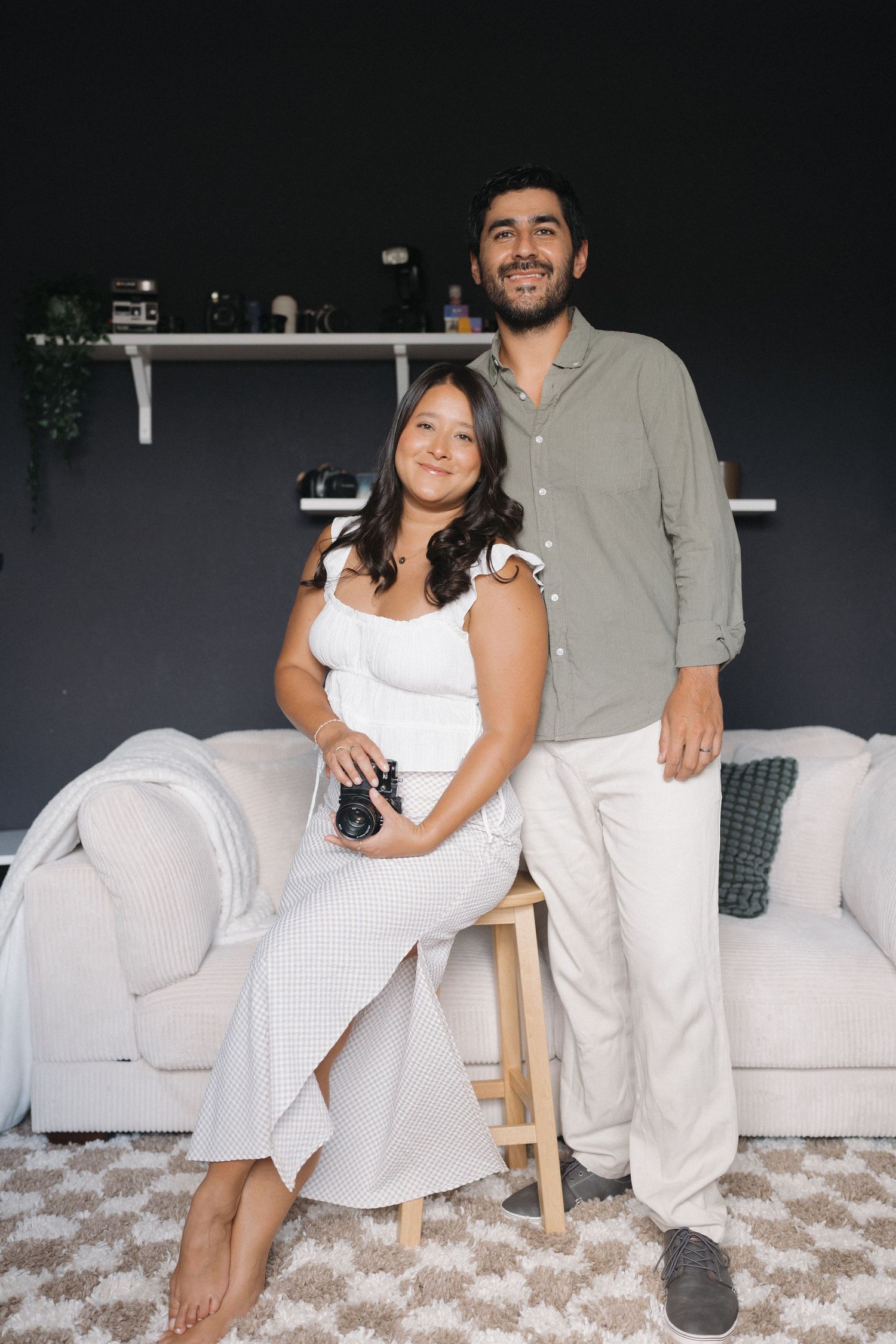 Casual lifestyle portrait of a couple in neutral clothing sitting on white couch.