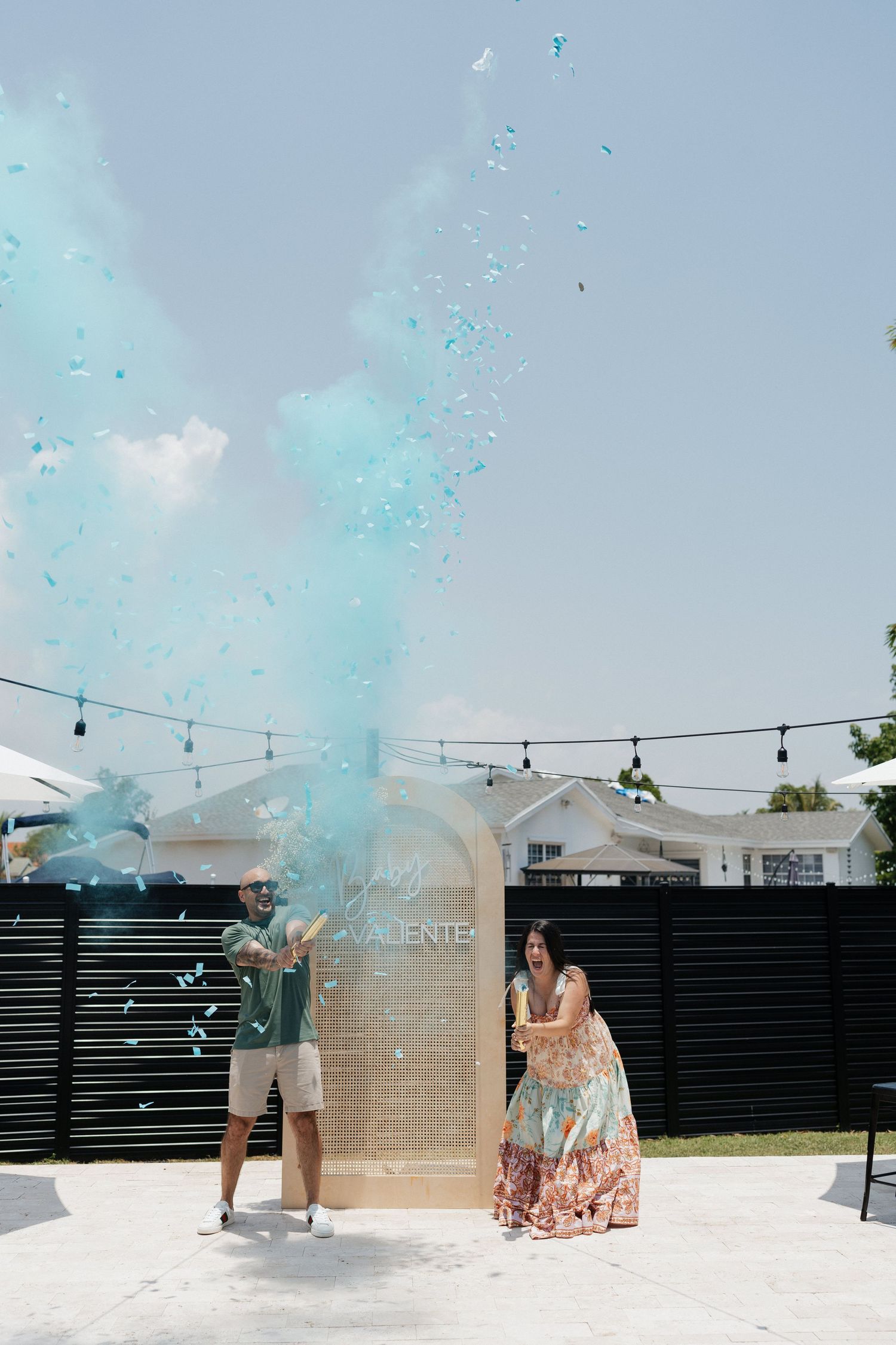 Gender reveal party moment with blue powder explosion in outdoor backyard setting.
