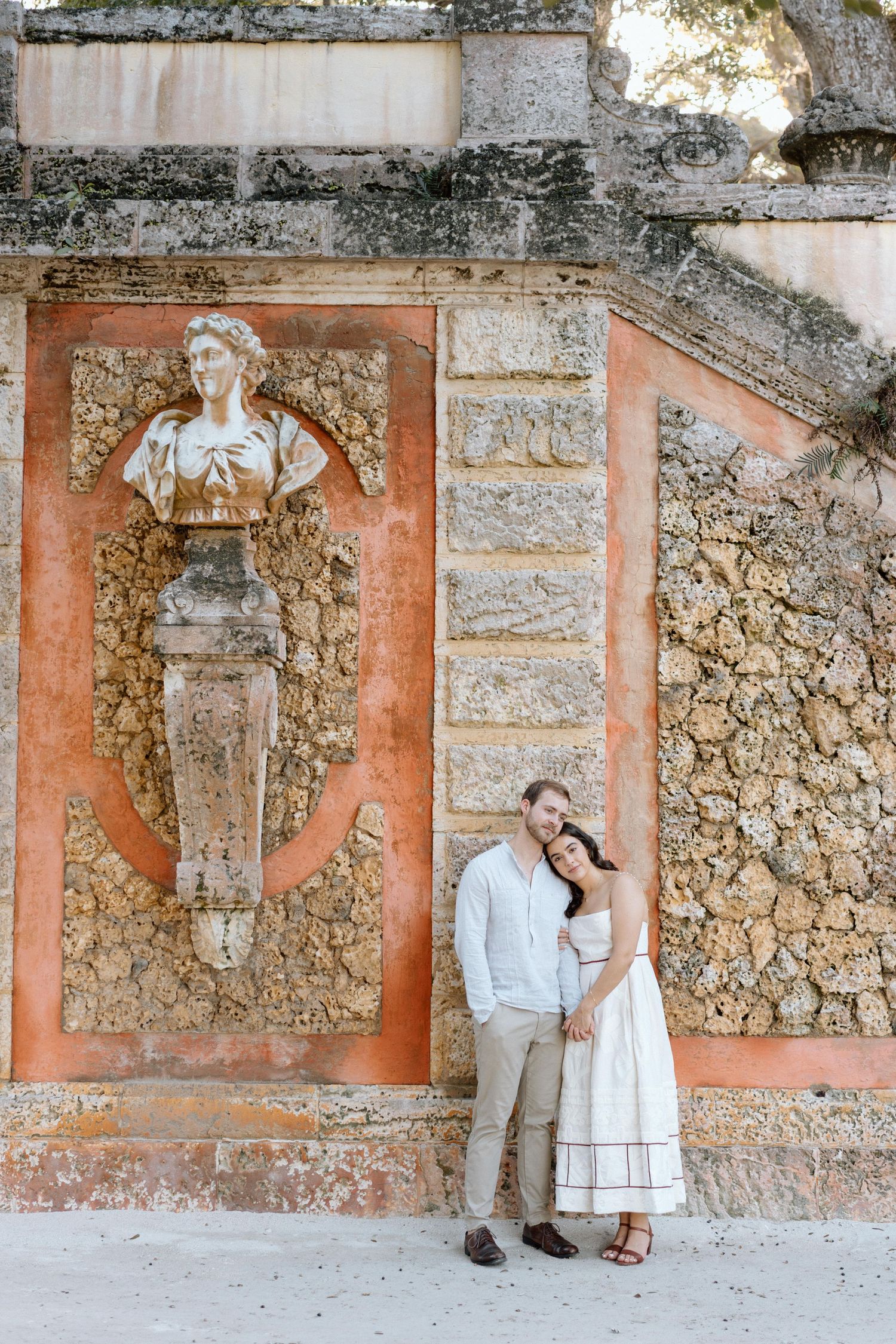 A couple poses by a terracotta wall featuring classical architectural details and carved figures.