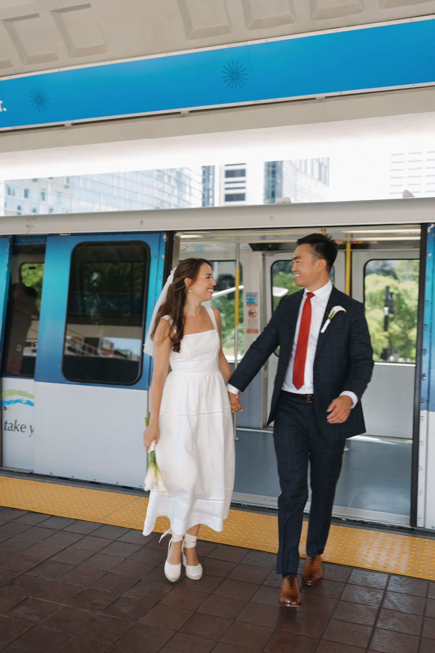 Wedding couple posing playfully by blue and white metro train.
