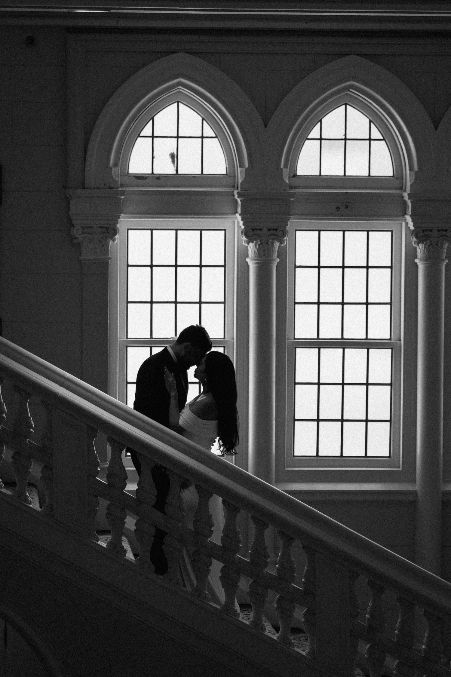 A silhouetted couple shares an intimate moment against arched windows on a grand staircase.