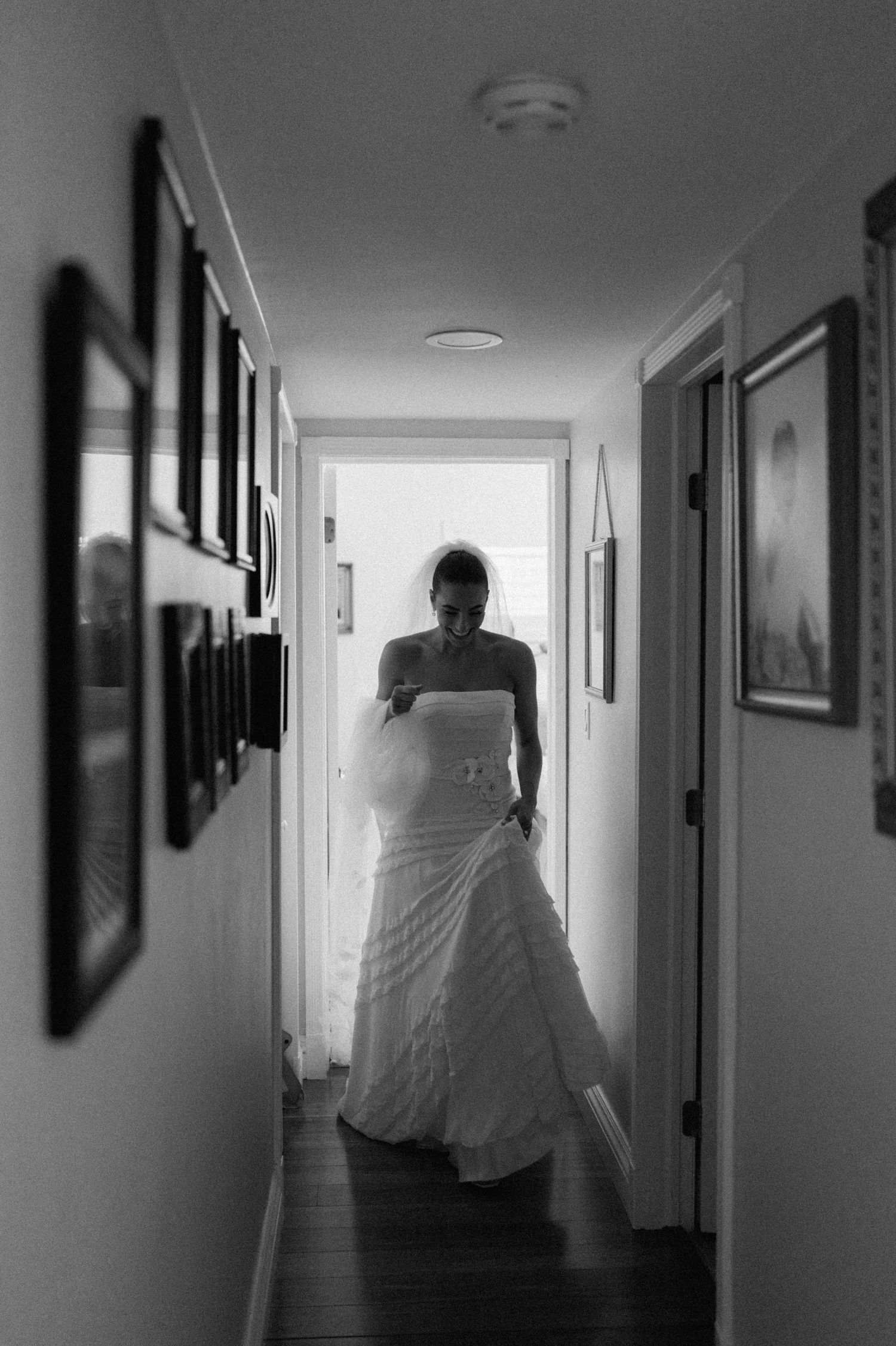 Silhouette of bride in wedding dress standing in hallway with framed photos.