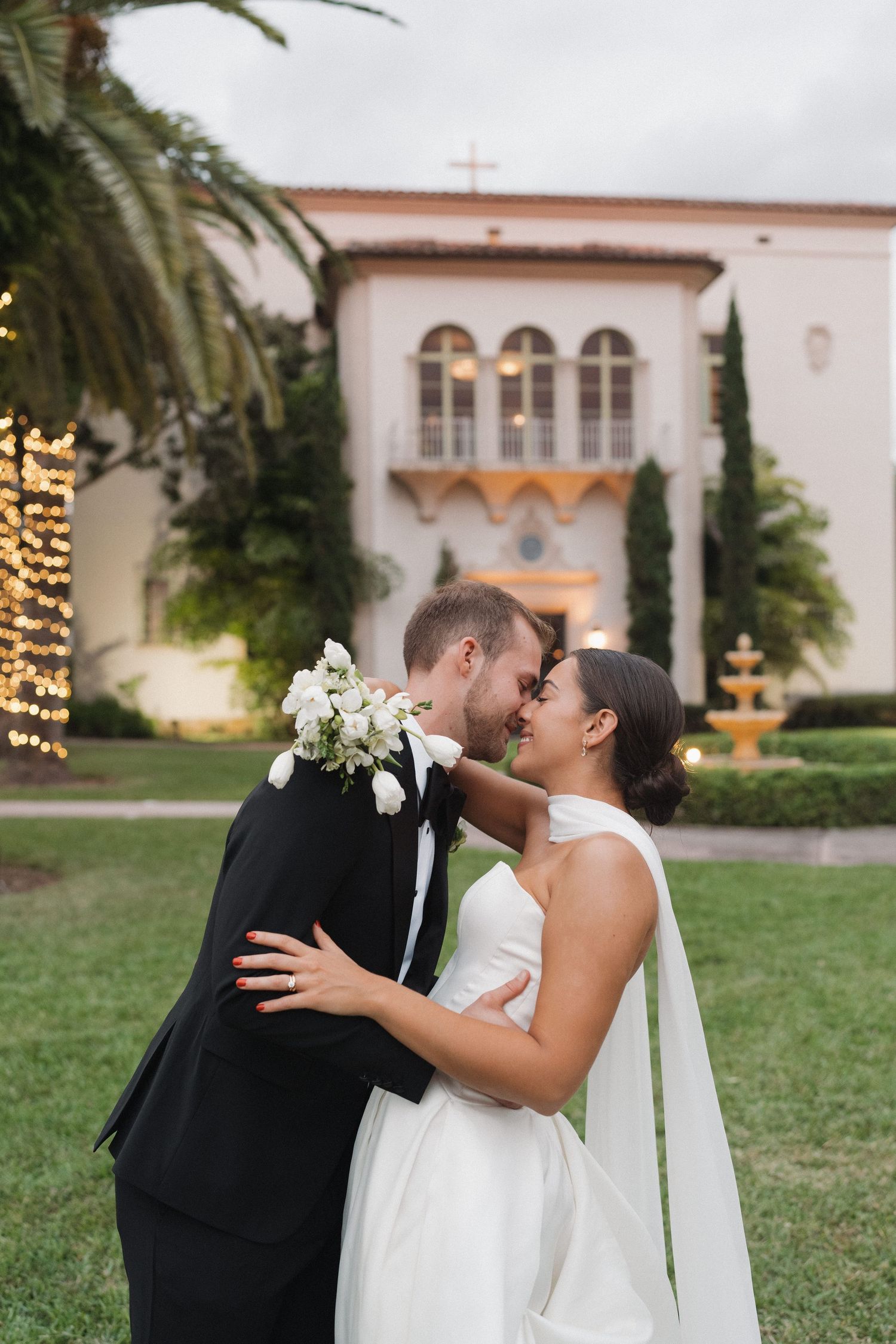 Romantic garden wedding portrait in front of Mediterranean-style architecture with palm trees.
