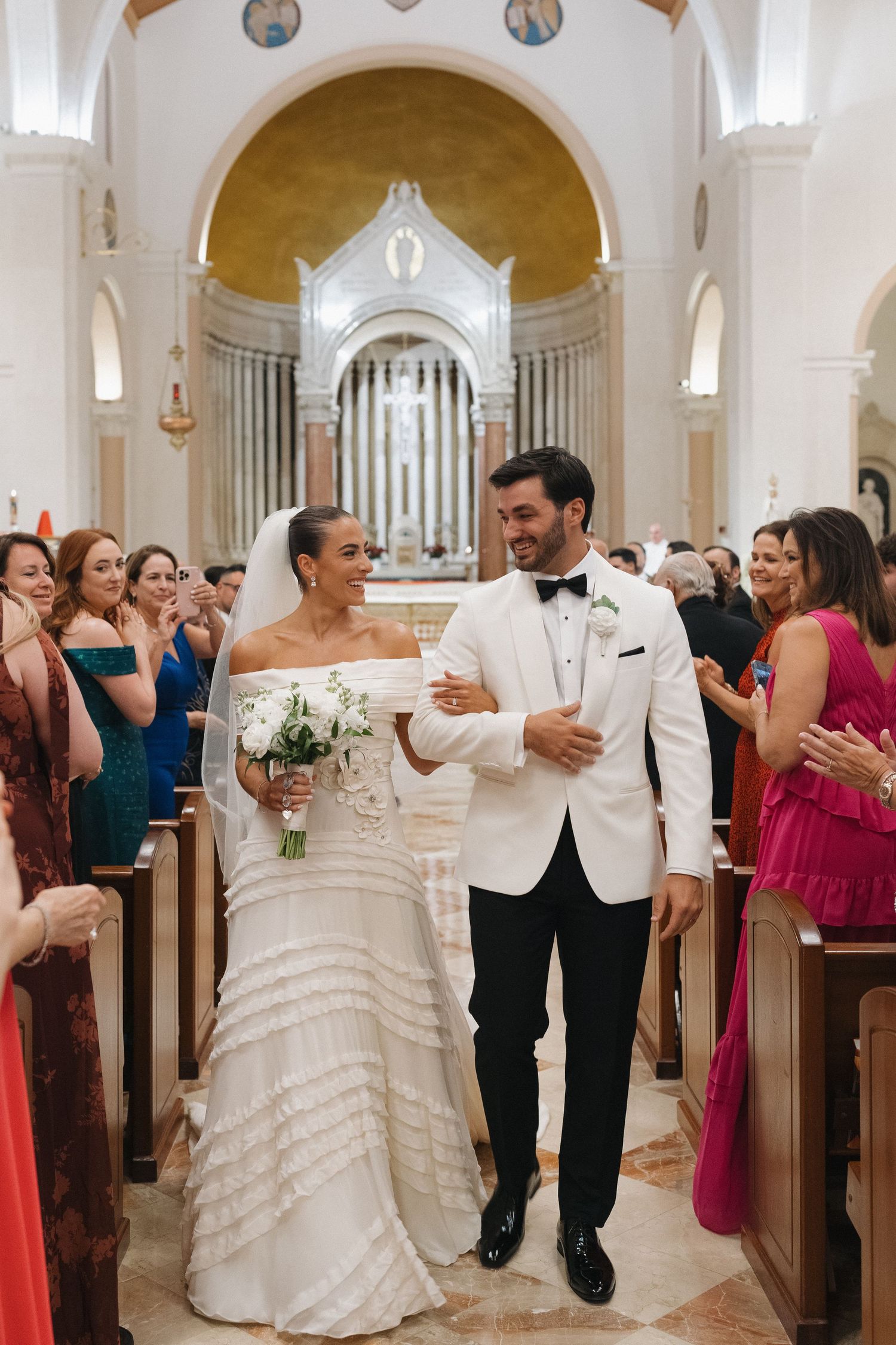 Church wedding ceremony exit with guests in colorful attire lining the aisle.