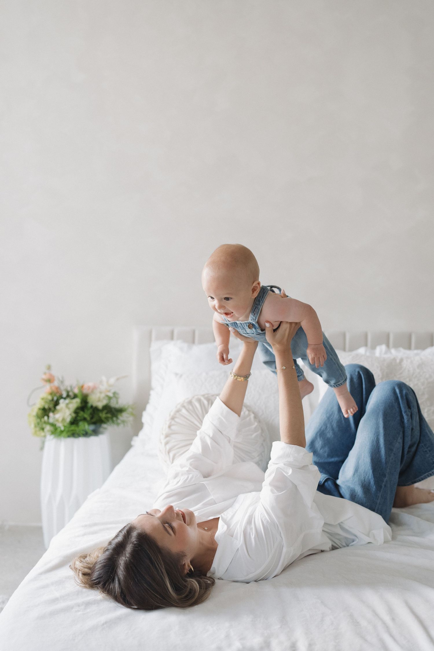 Playful parenting moment on white bedding in bright minimalist bedroom.