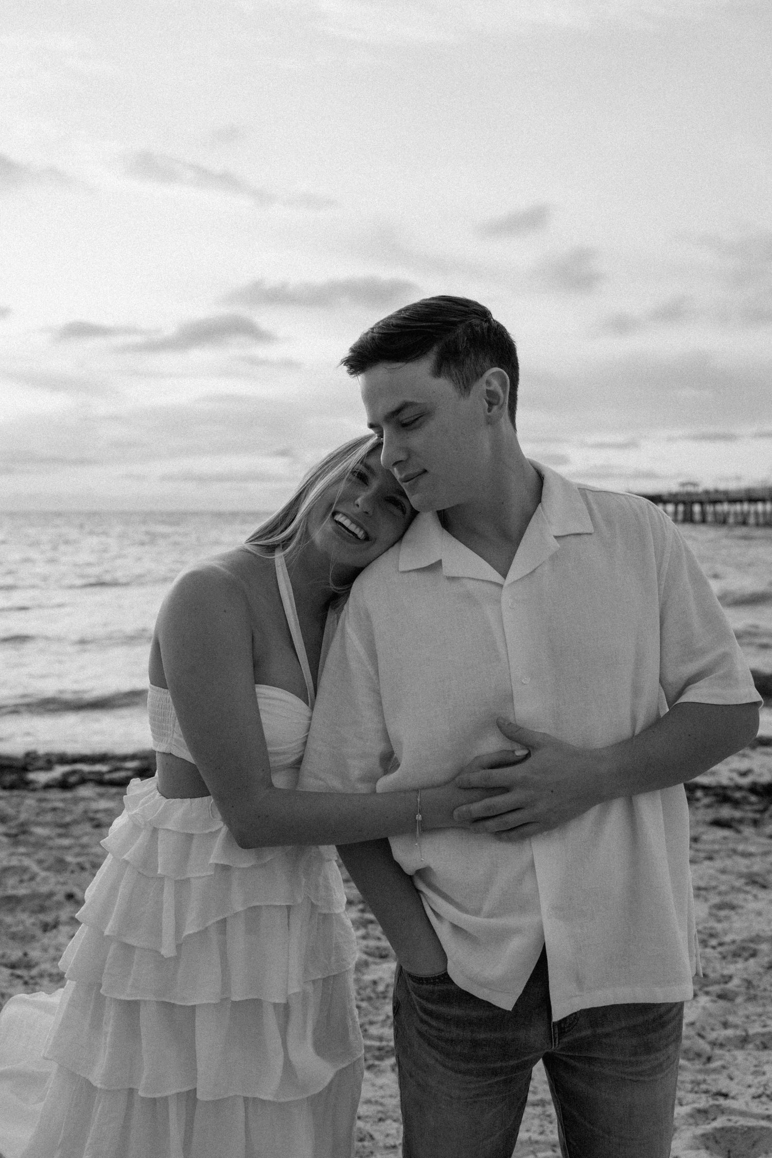 A black and white portrait of a couple sharing a tender moment on the beach.