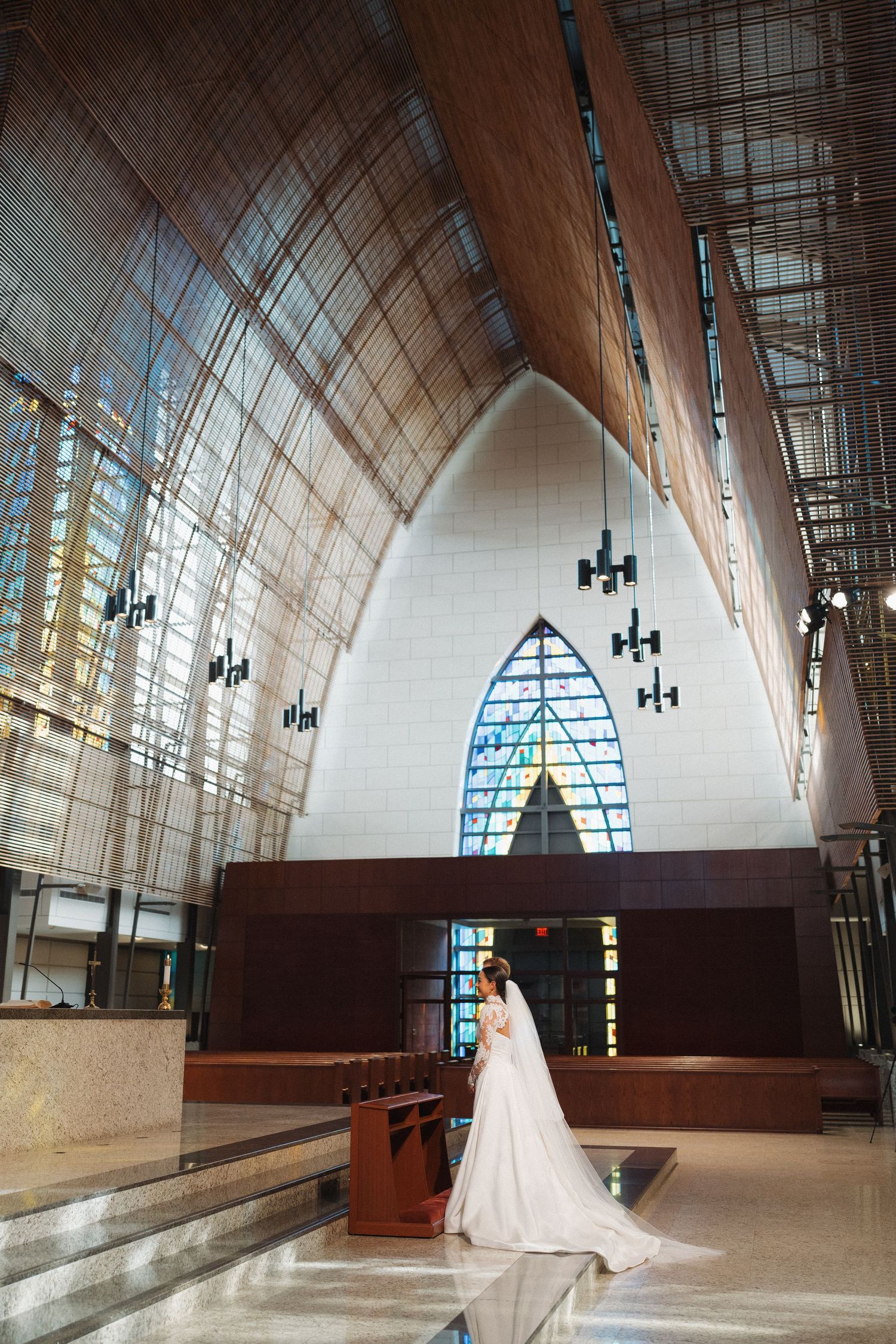 A wedding ceremony in a modern church with dramatic vaulted ceilings, stained glass windows, and hanging chandeliers.