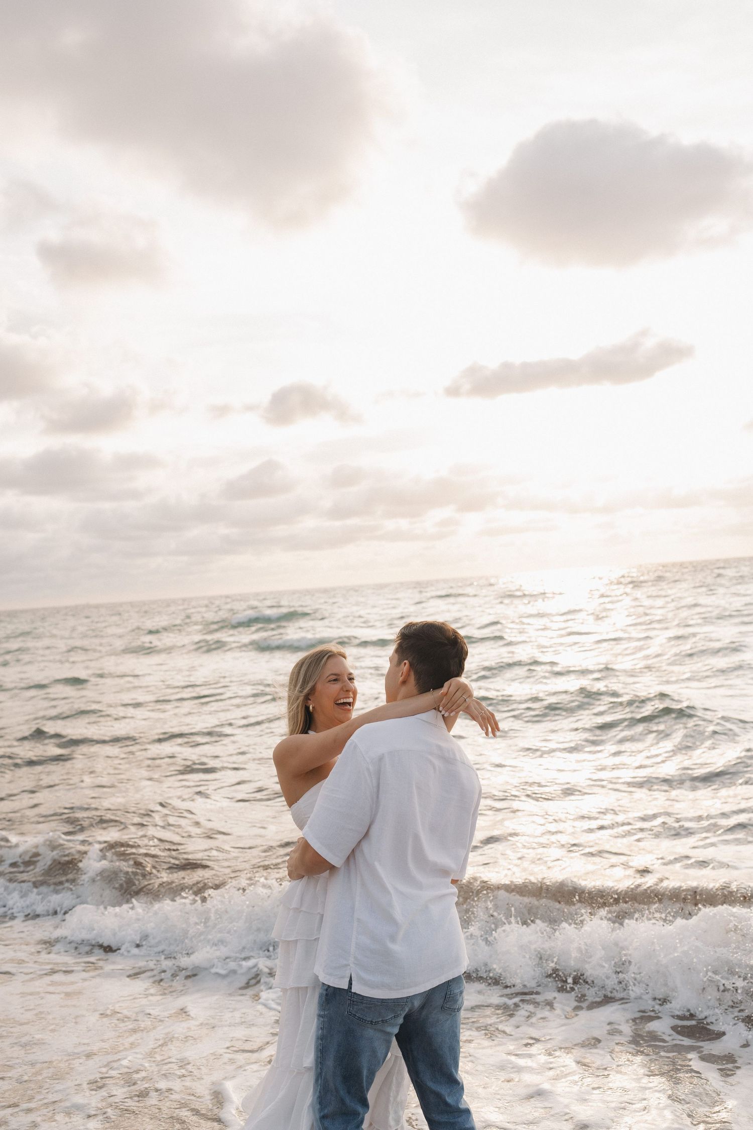 Romantic couple embracing in the ocean waves during a sunset beach photoshoot.