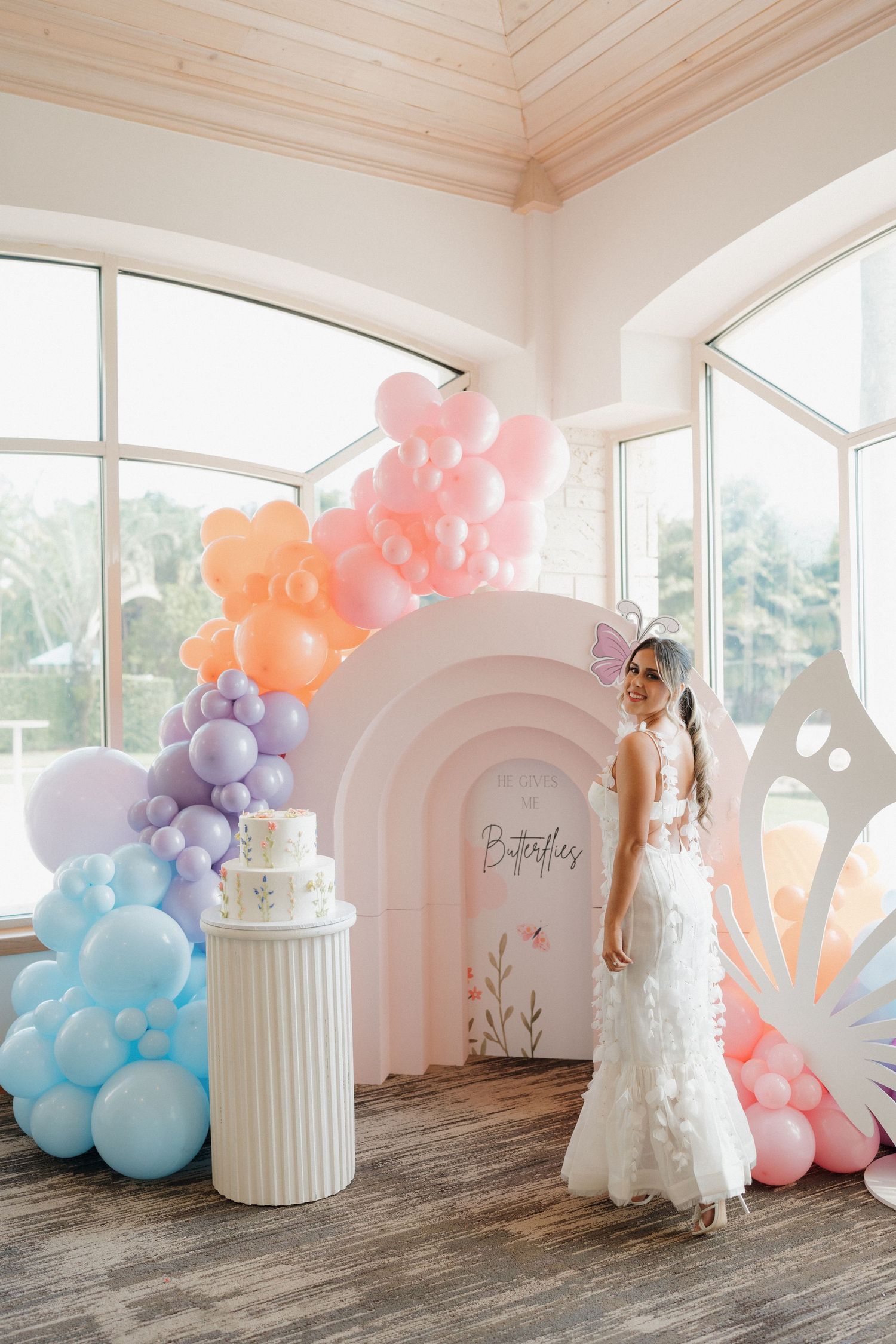 Pastel rainbow balloon arch installation with decorative white column and arch backdrop.