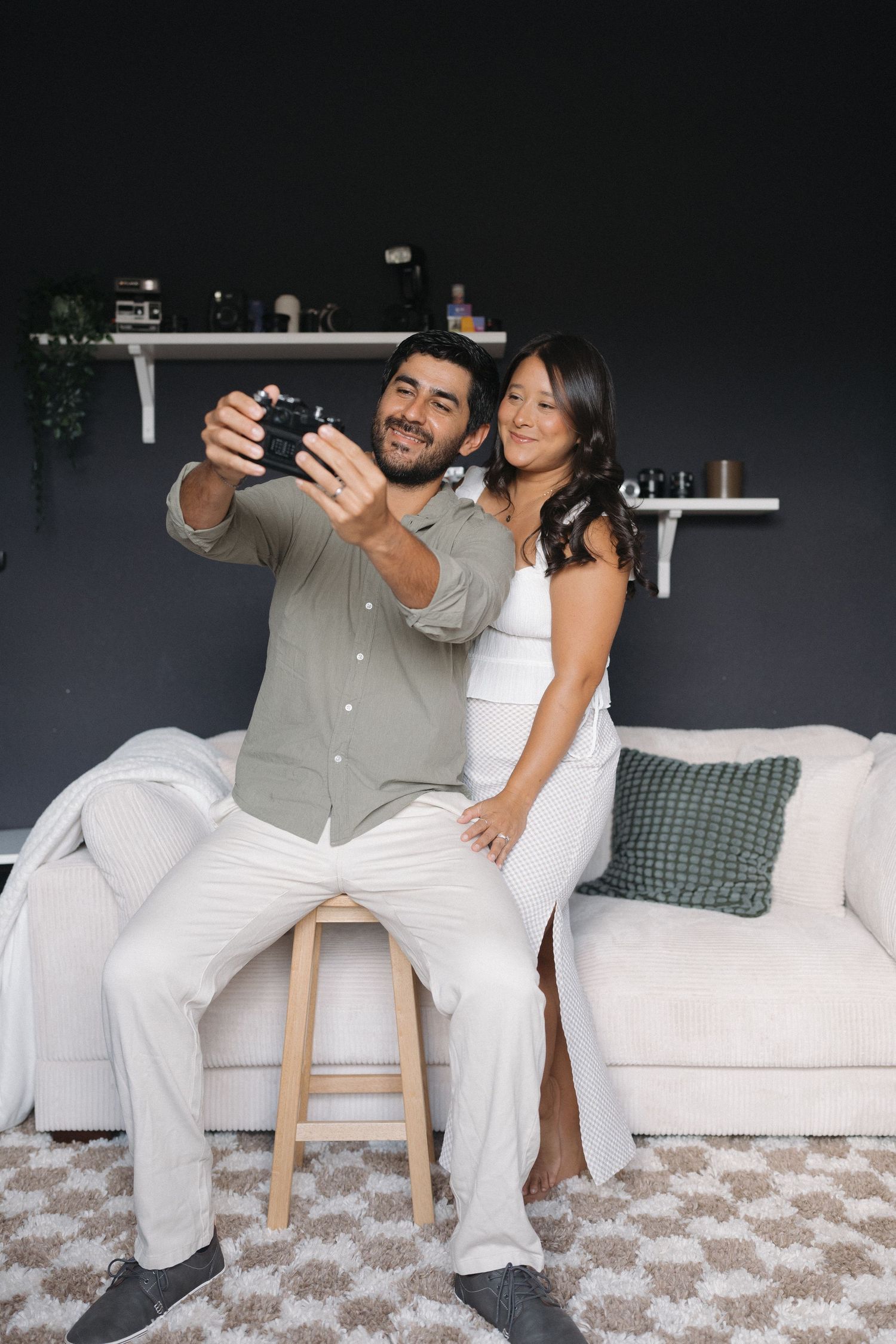 Couple taking selfie while sitting on white couch in casual home setting.