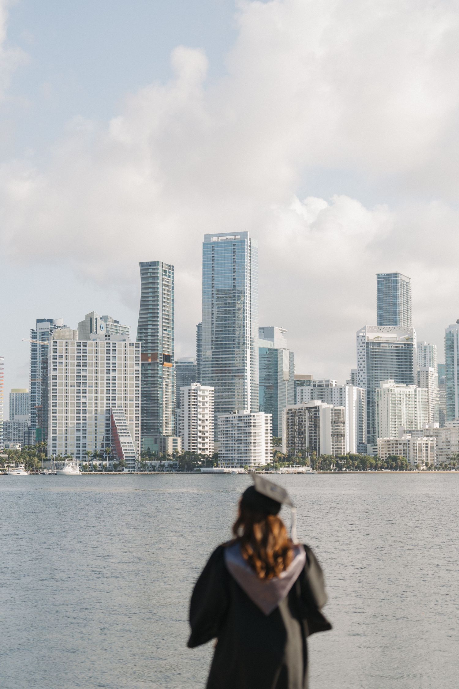 Graduate overlooking Miami skyline and waterfront in graduation attire.