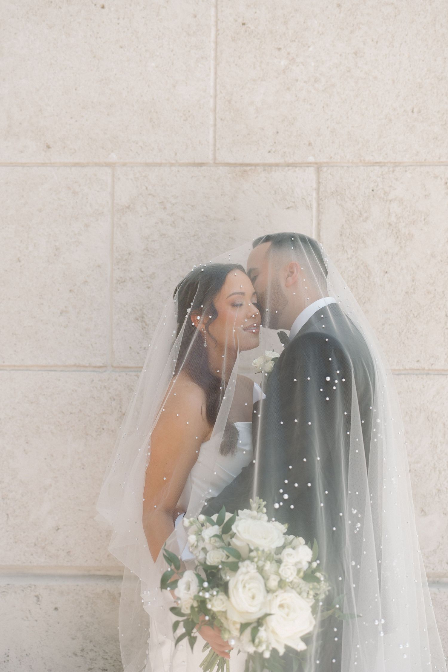 Intimate wedding portrait with white bouquet against stone wall with sparkle overlay effect.