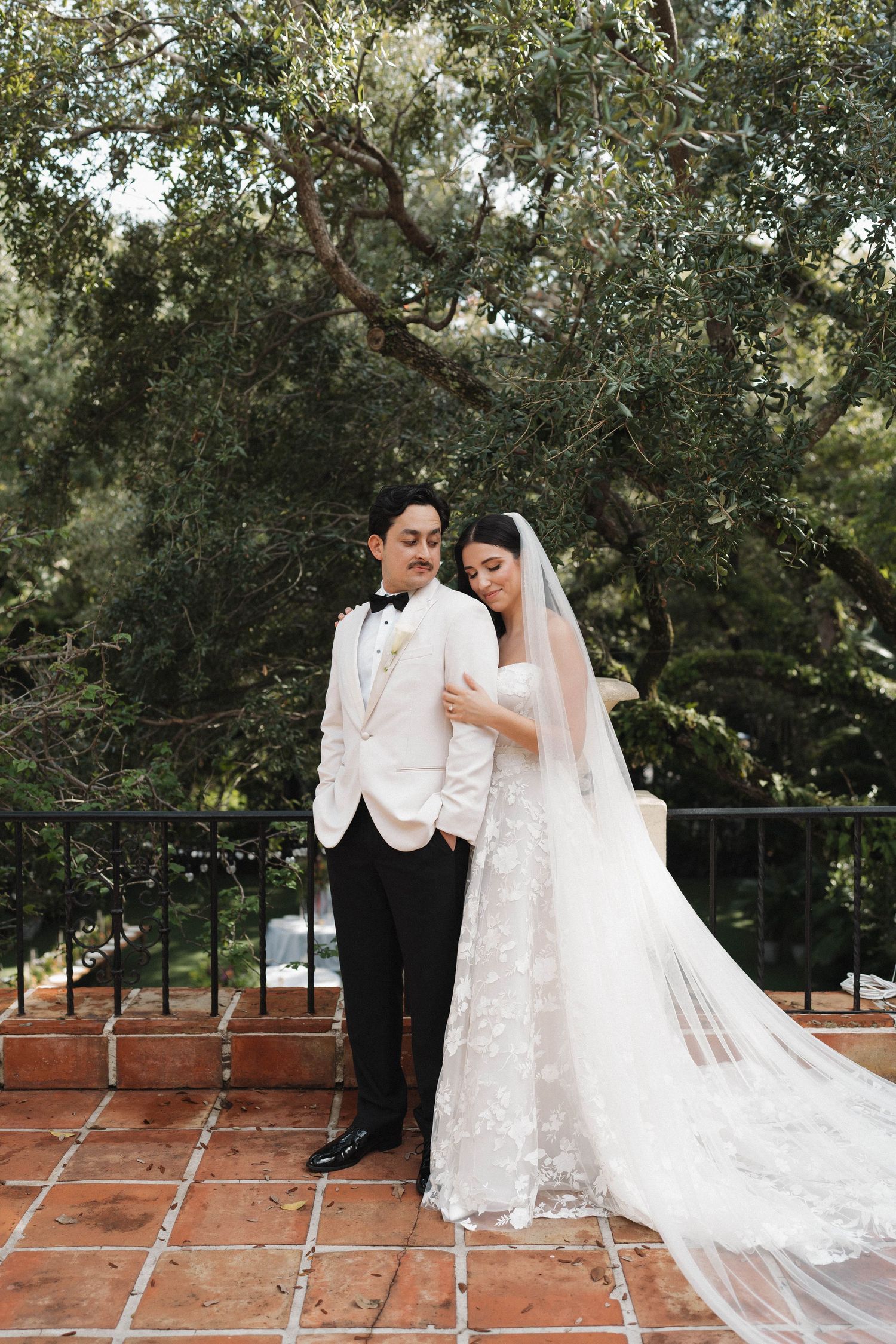 A wedding couple shares an intimate moment on a brick patio surrounded by lush greenery.