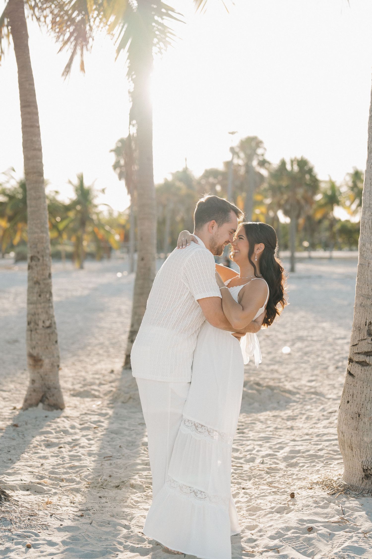 Romantic beach wedding photos with palm trees and golden sunlight filtering through.