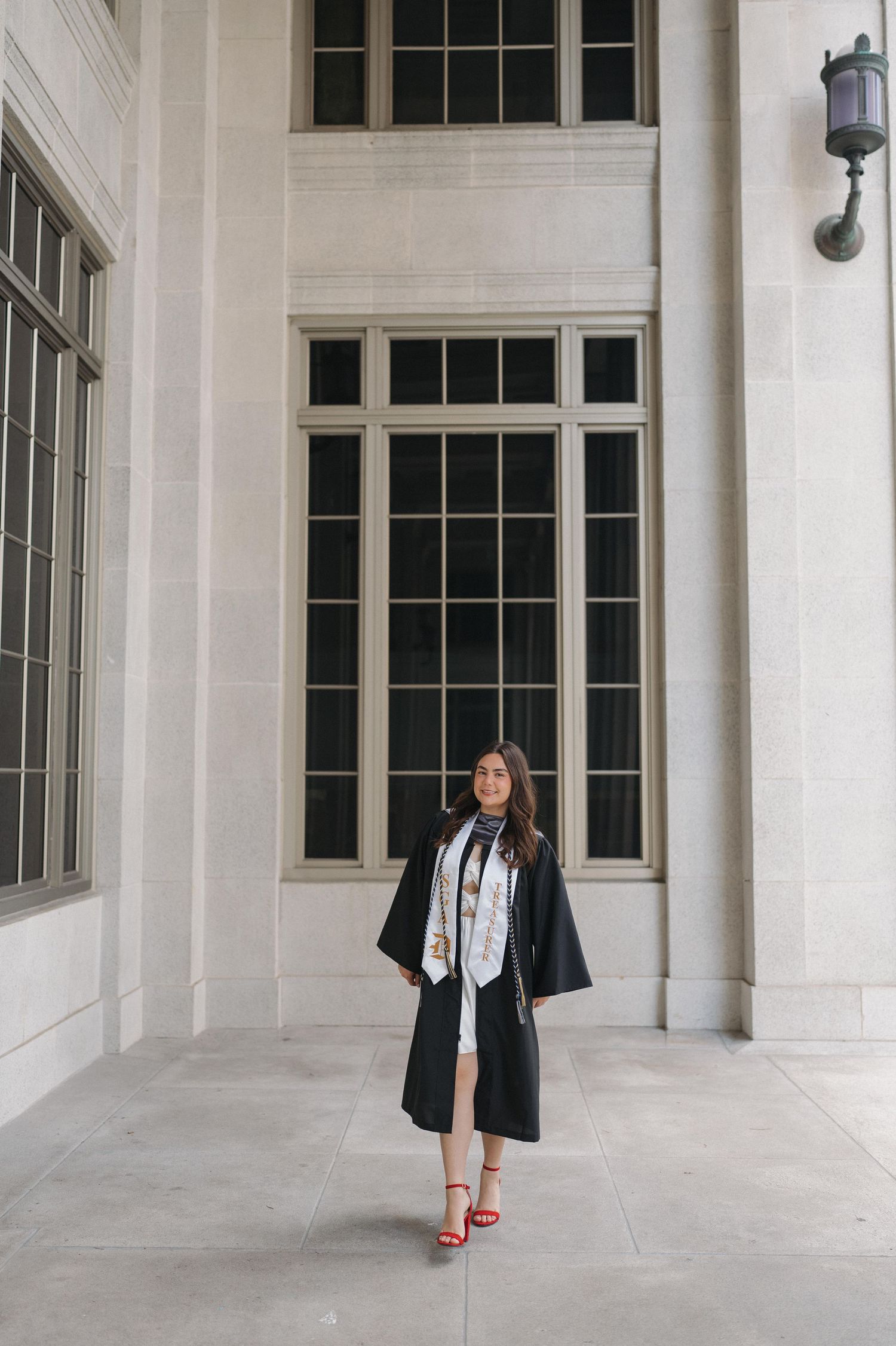 Woman in graduation attire poses in front of classical columned building.