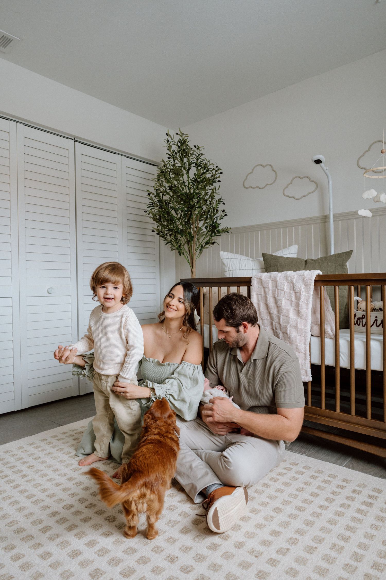 Family plays together with their golden retriever dog in bright white nursery room.
