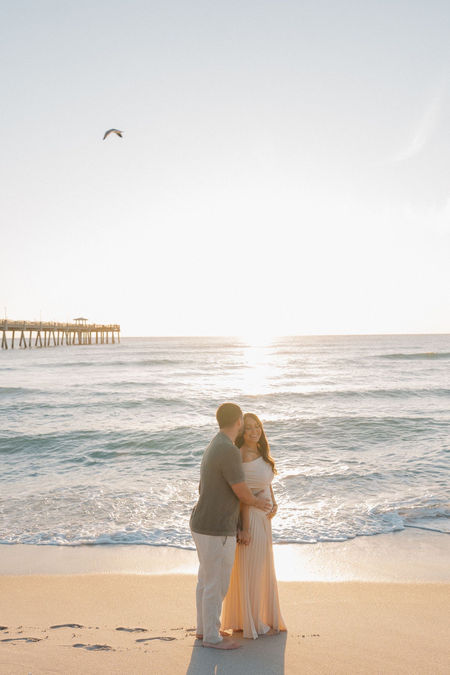 A peaceful sunset beach scene with waves rolling onto shore and a pier in the distance.