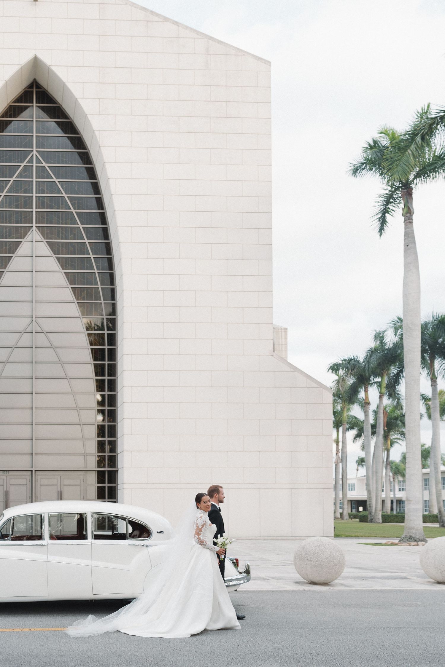 Modern white church exterior with palm trees and classic car creating an elegant wedding scene.