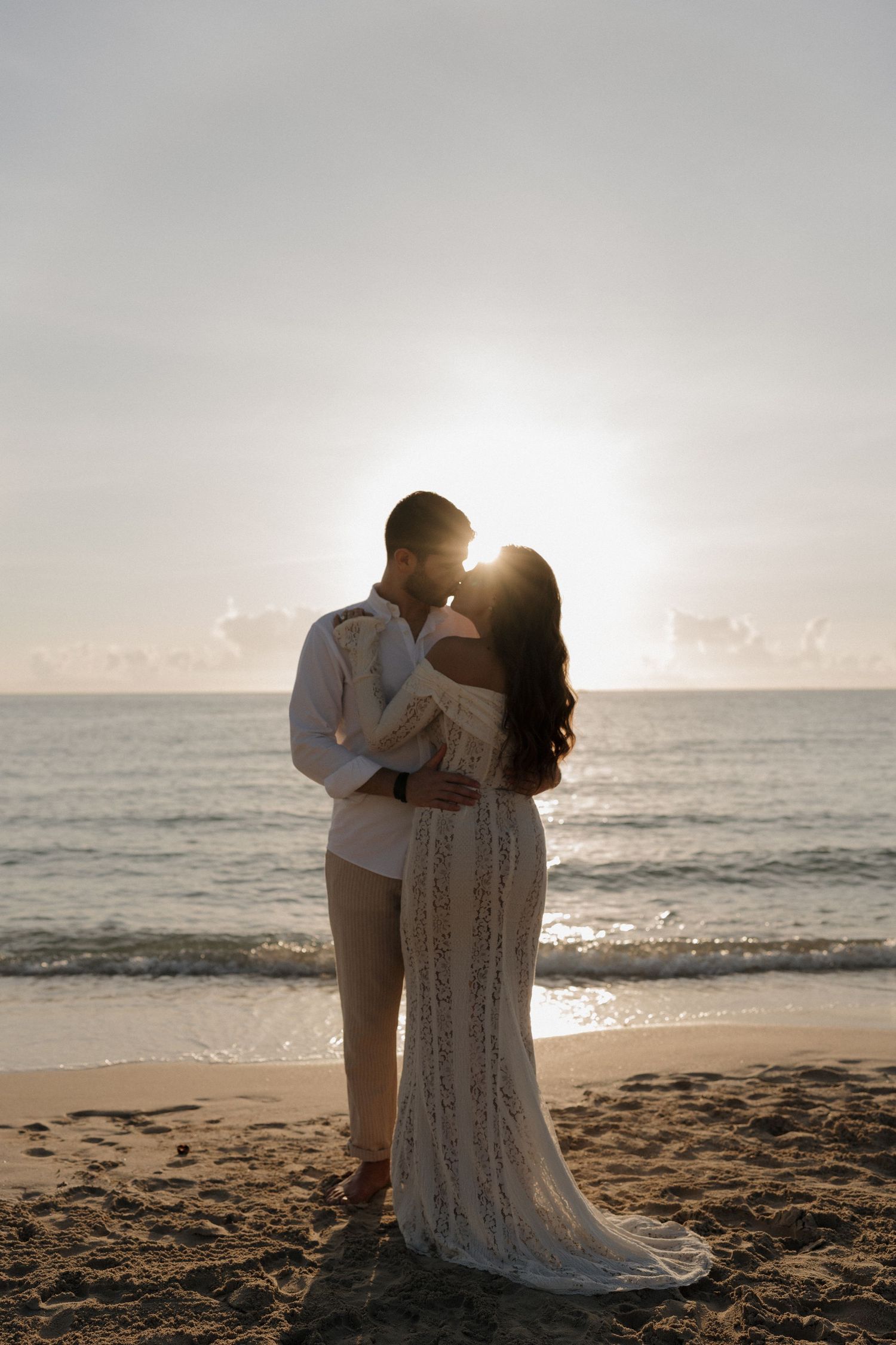 A couple shares an intimate moment on the beach with the sun creating a beautiful backlight silhouette.