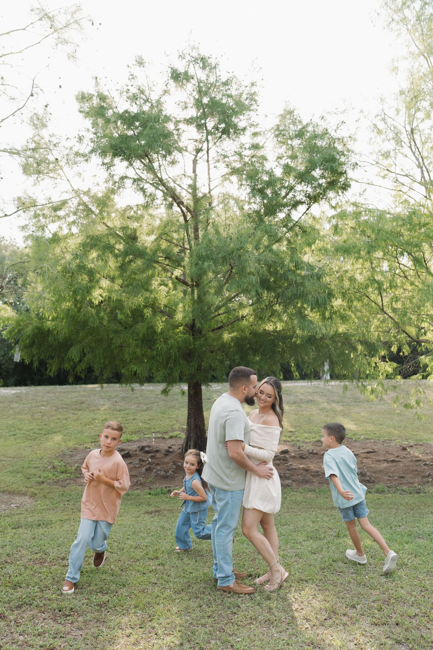 A playful family moment under a large tree in a grassy park during sunset.