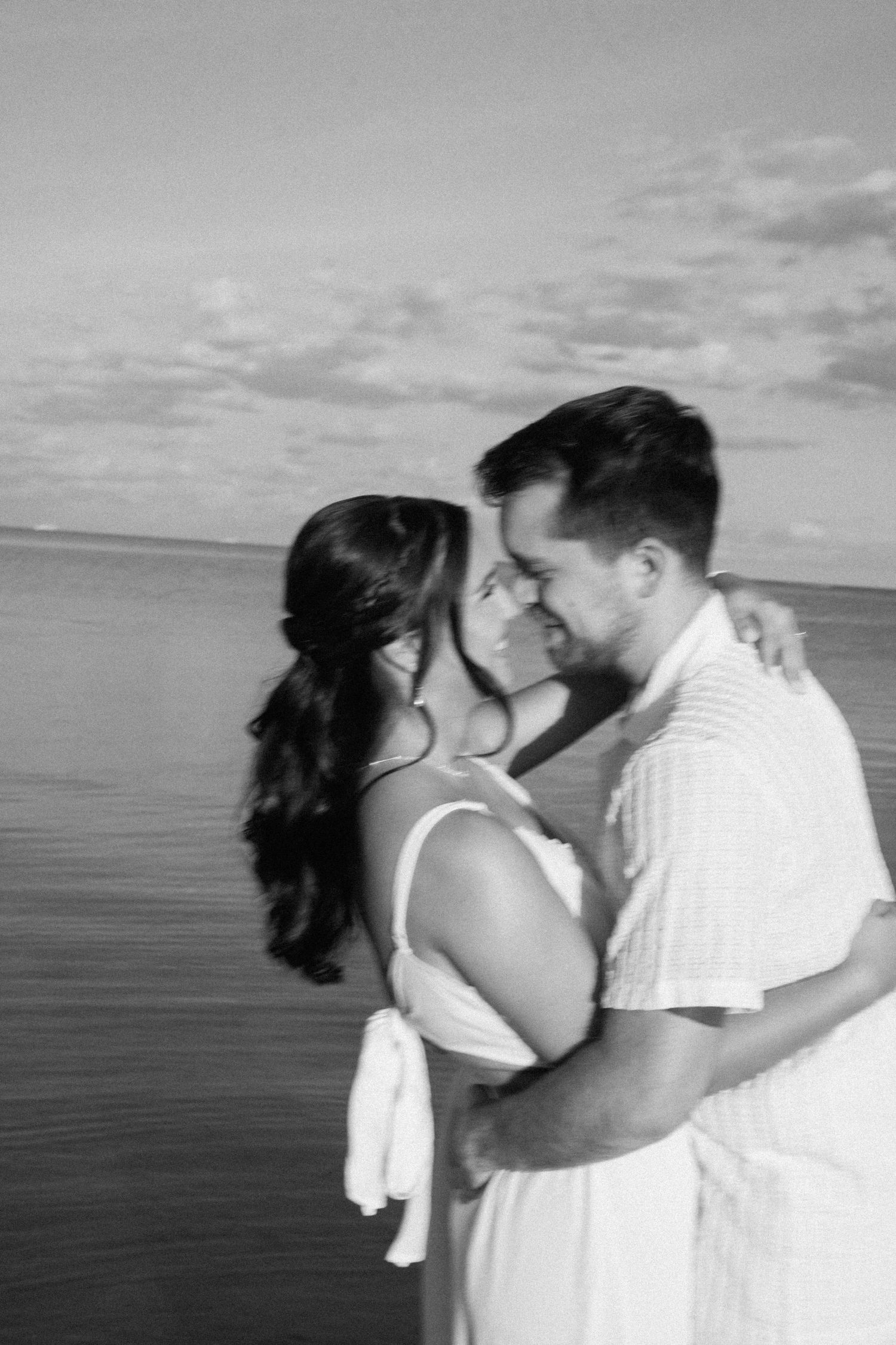 Black and white beach portraits capturing intimate moments against an ocean backdrop.