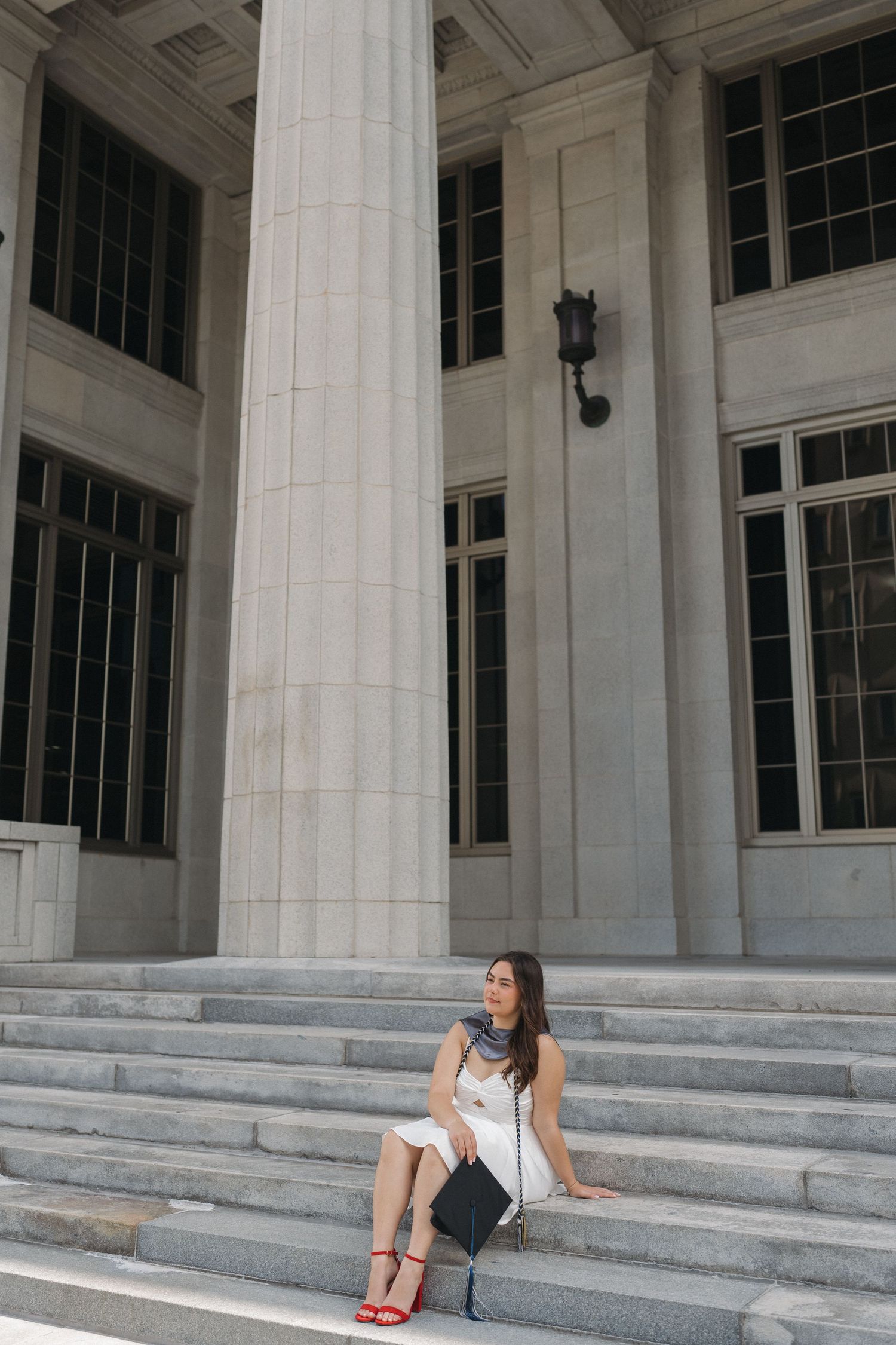 Woman in casual attire sits on grand stone steps of classical building.
