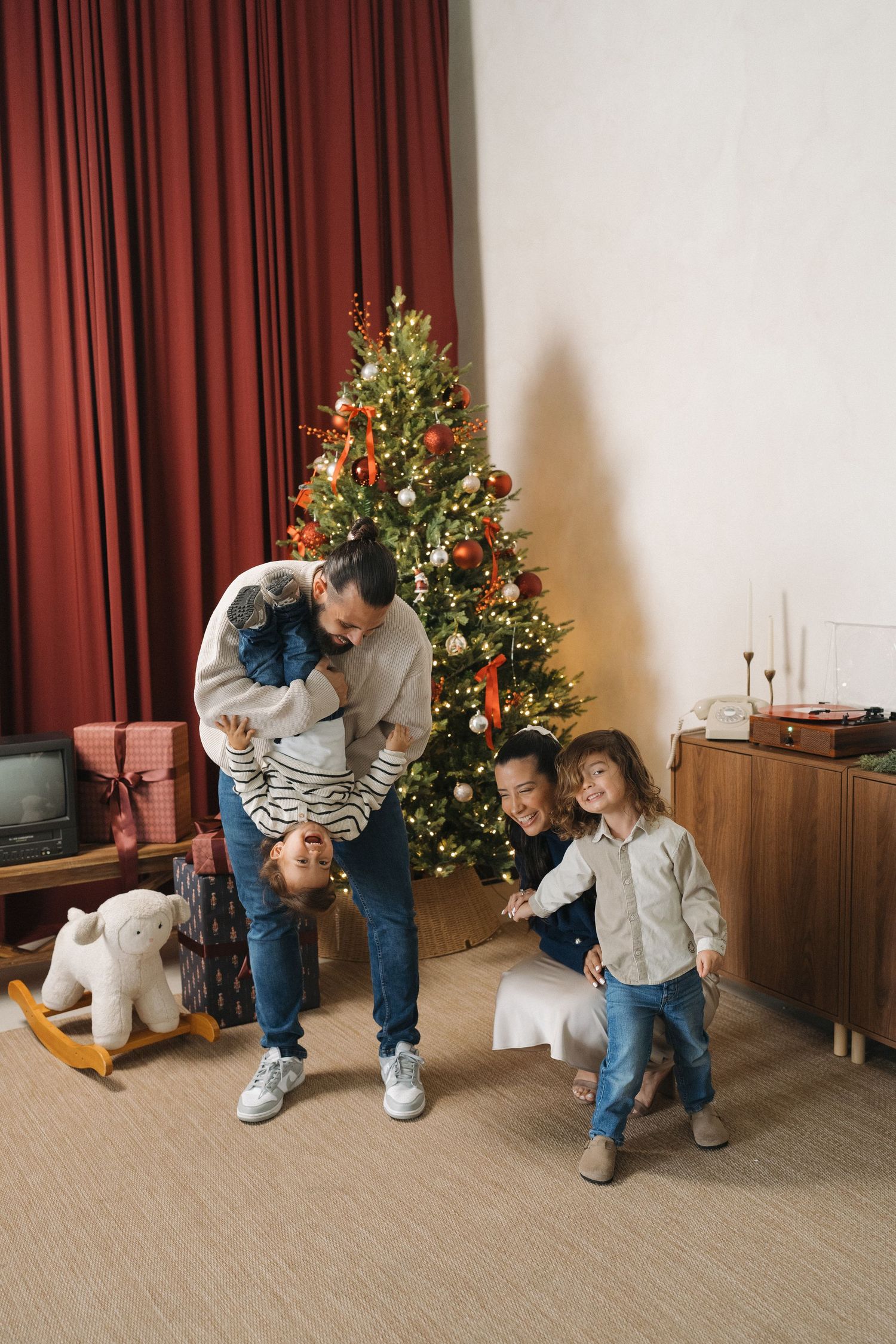 Family of four celebrating Christmas together near a decorated tree with gifts and festive decor in a cozy living room.
