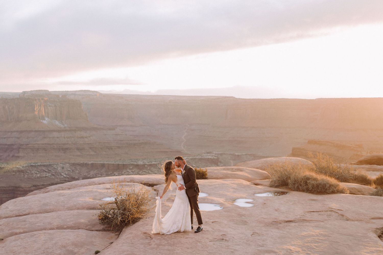 Wedding couple shares intimate moment at sunset on desert cliff overlook.