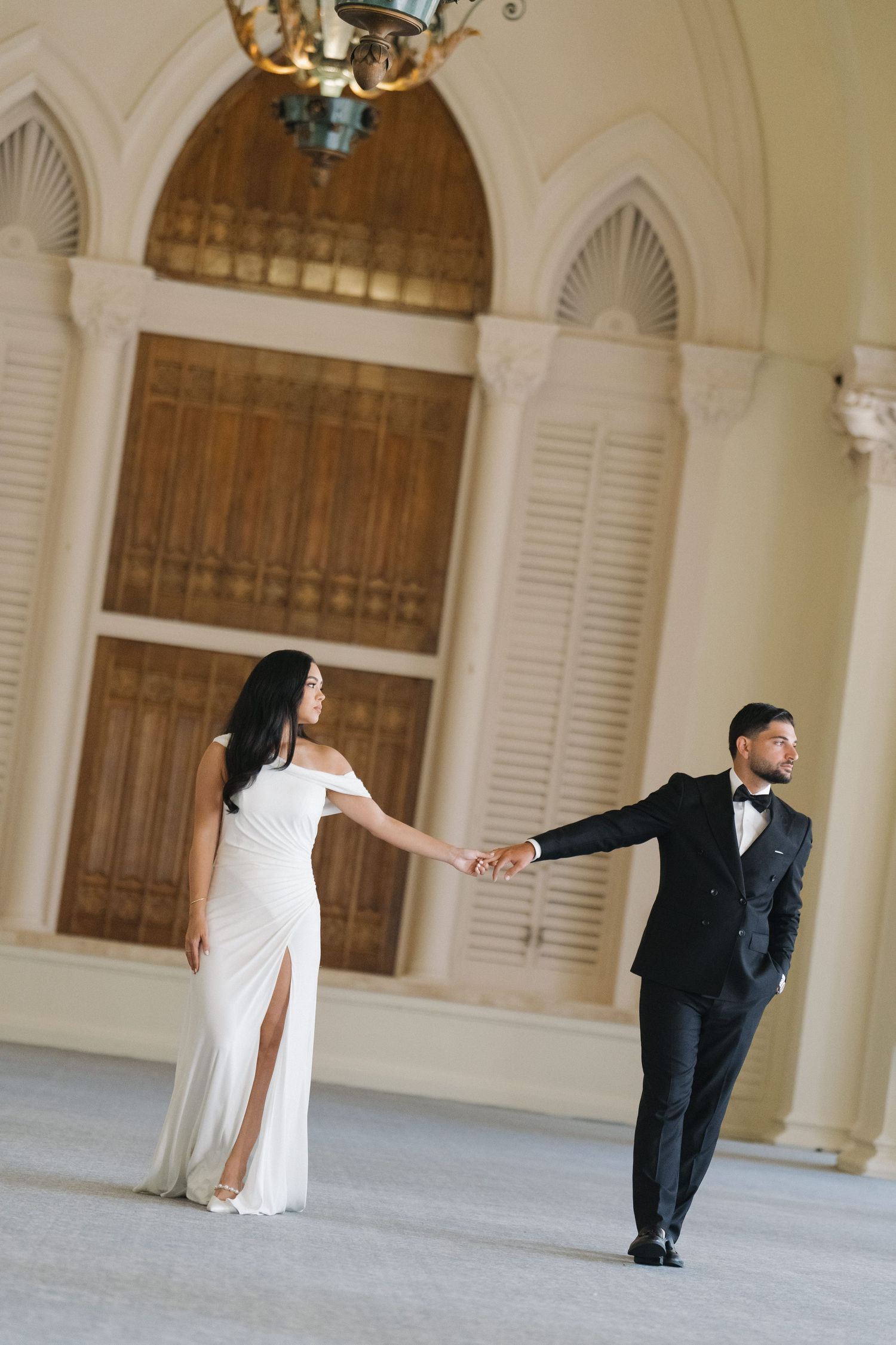 A playful wedding photoshoot in an elegant white hall with arched windows and shutters.