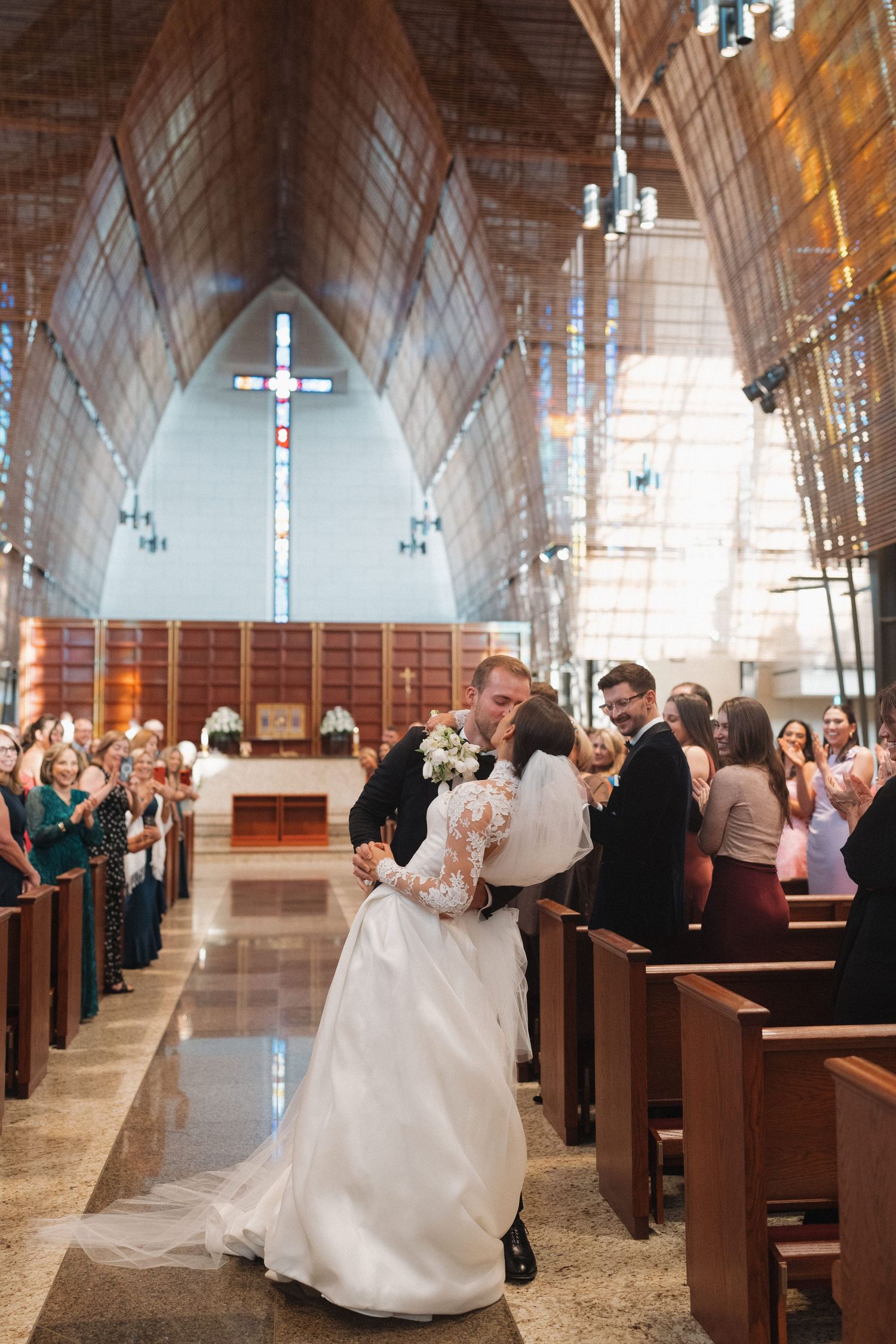 A wedding ceremony in progress inside a grand church with stained glass windows and wooden pews.