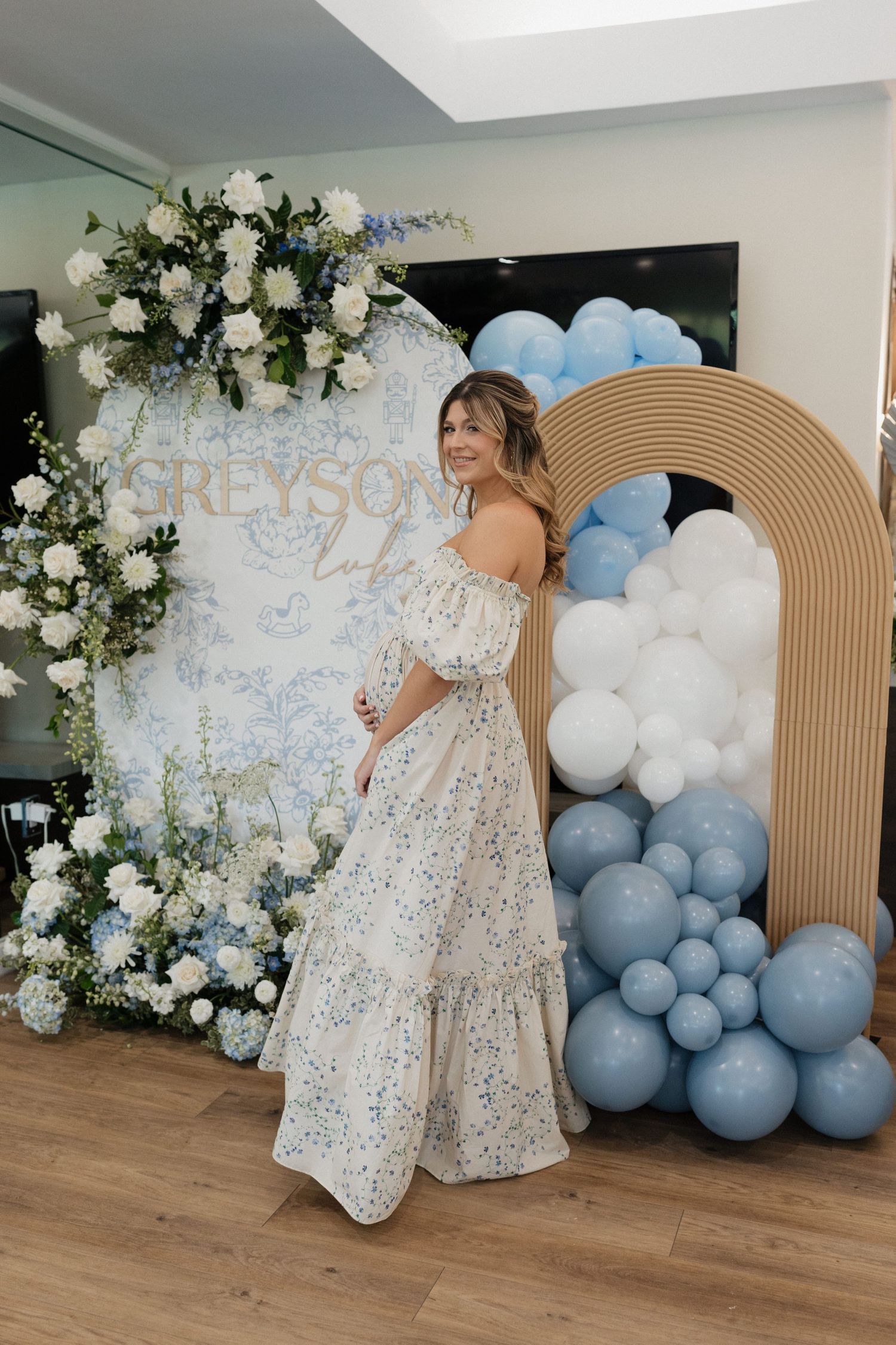 Decorative event space with white balloon garland, floral arrangements and tan arched backdrops.