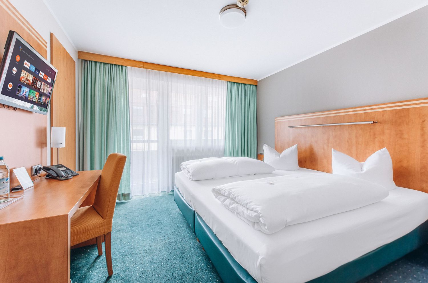 Hotel room with mint green curtains, wooden furnishings, and twin beds with white linens.