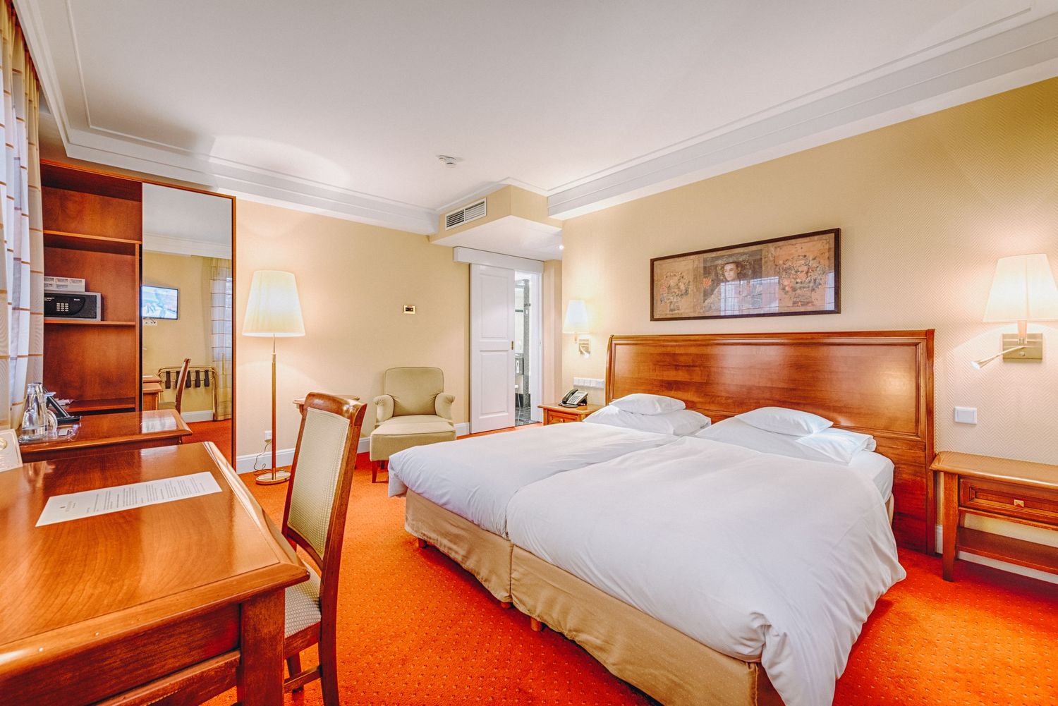 Luxurious hotel room with warm wood furnishings, beige walls, and bright red carpeting.