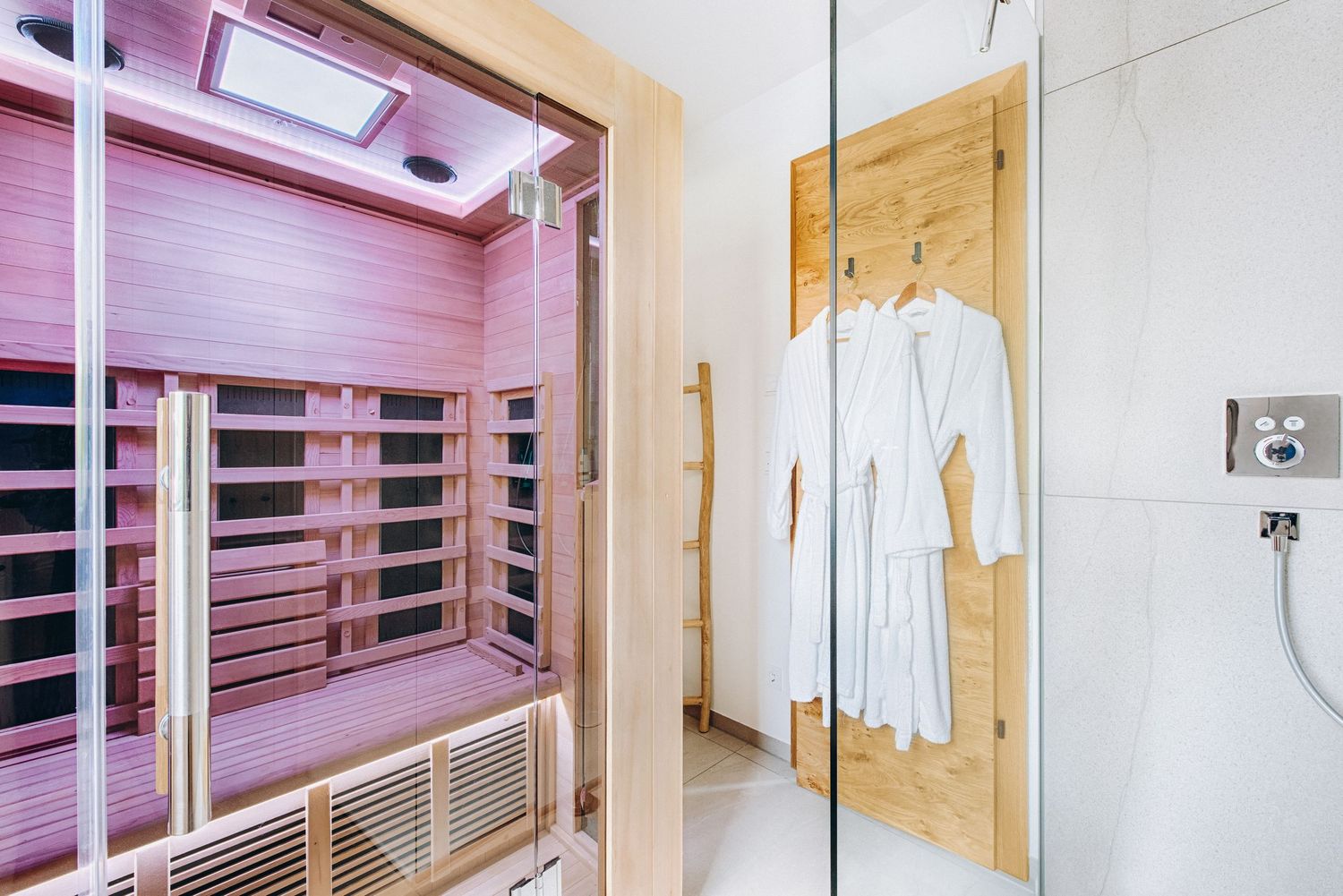 Modern bathroom interior with pink infrared sauna cabin and white bathrobe hanging on wooden door panel.