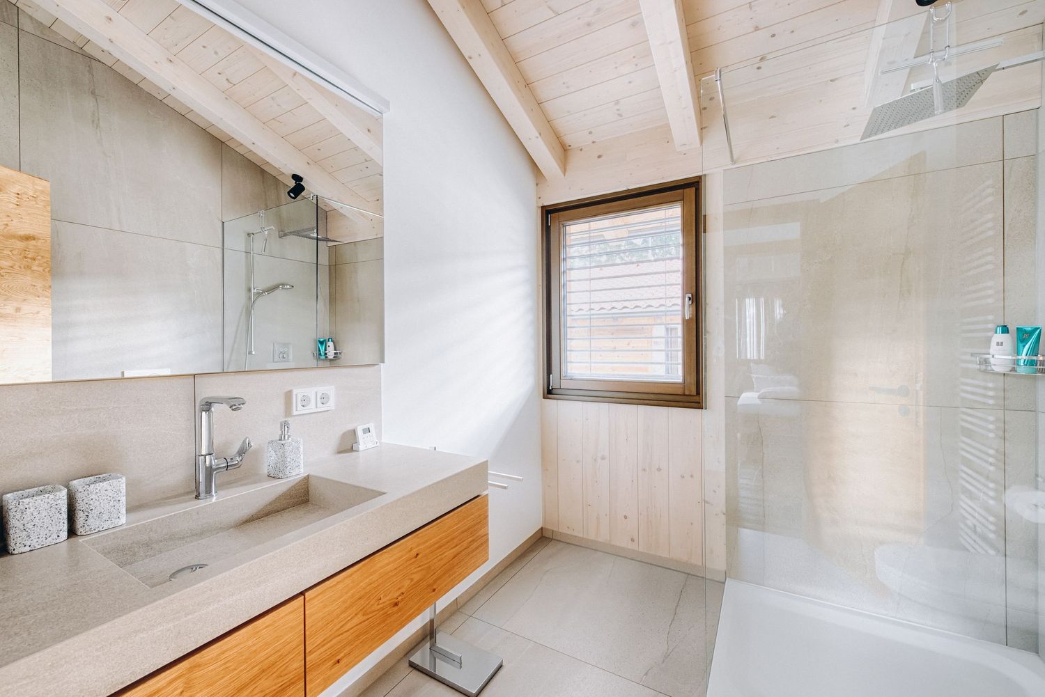 Modern minimalist bathroom with white walls, sloped ceiling, wooden accents and glass shower enclosure.